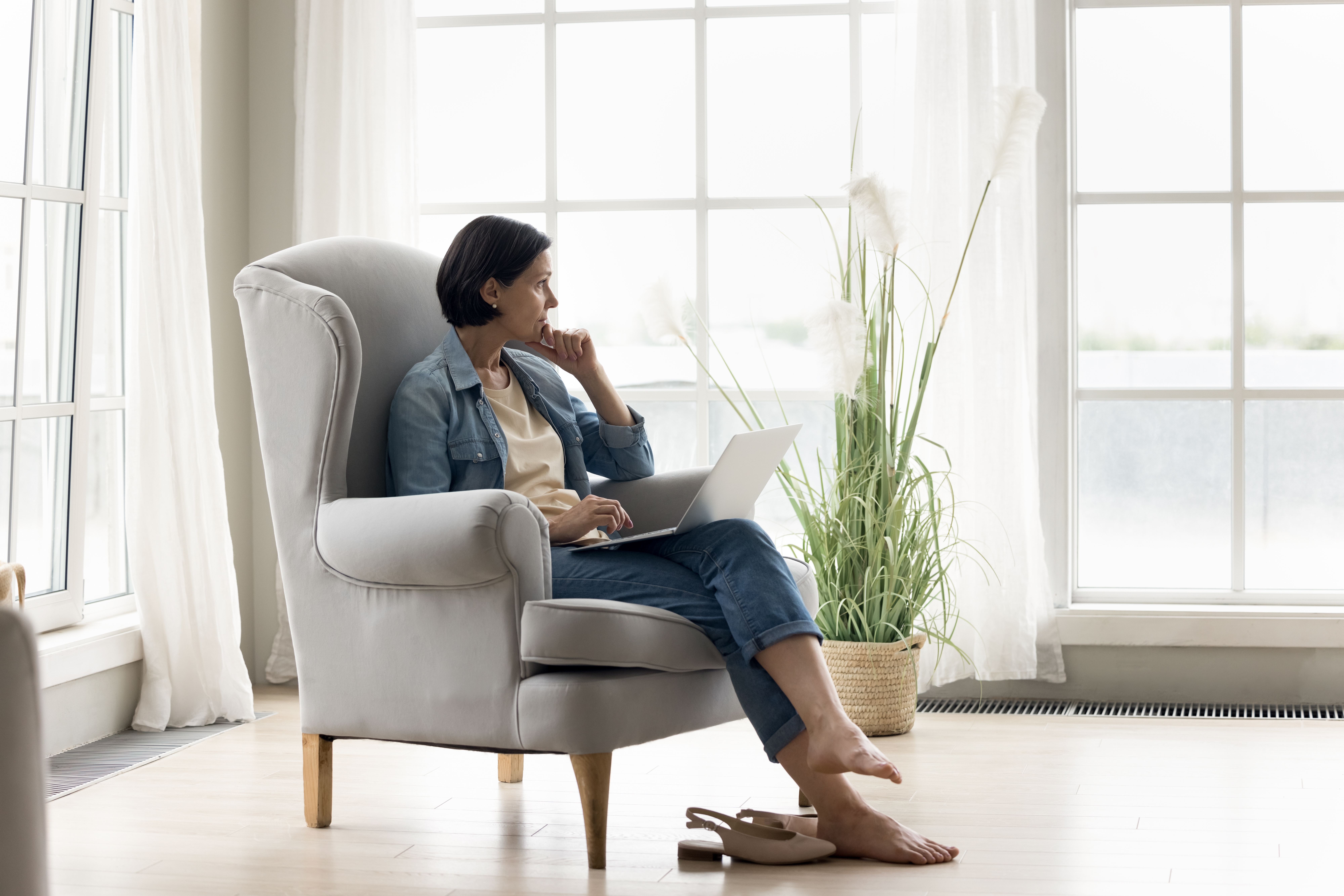 Woman looking out the window as she sits on a chair with her laptop | Source: Shutterstock