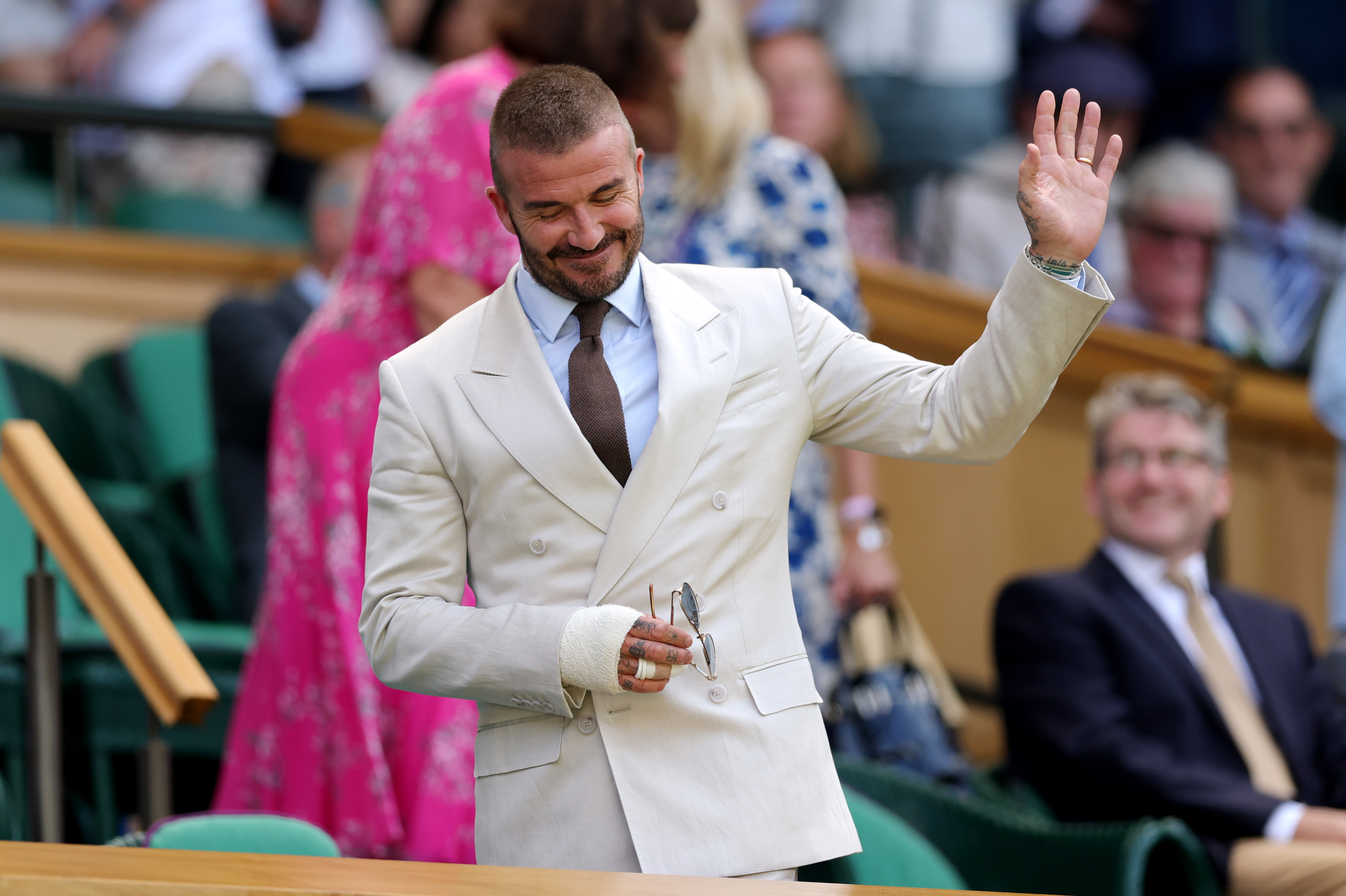 David Beckham steps into the Royal Box at Wimbledon, greeted by applause. With a modest wave and subtle smile, he keeps his signature cool — even with his hand in a wrap and sunglasses in tow.
