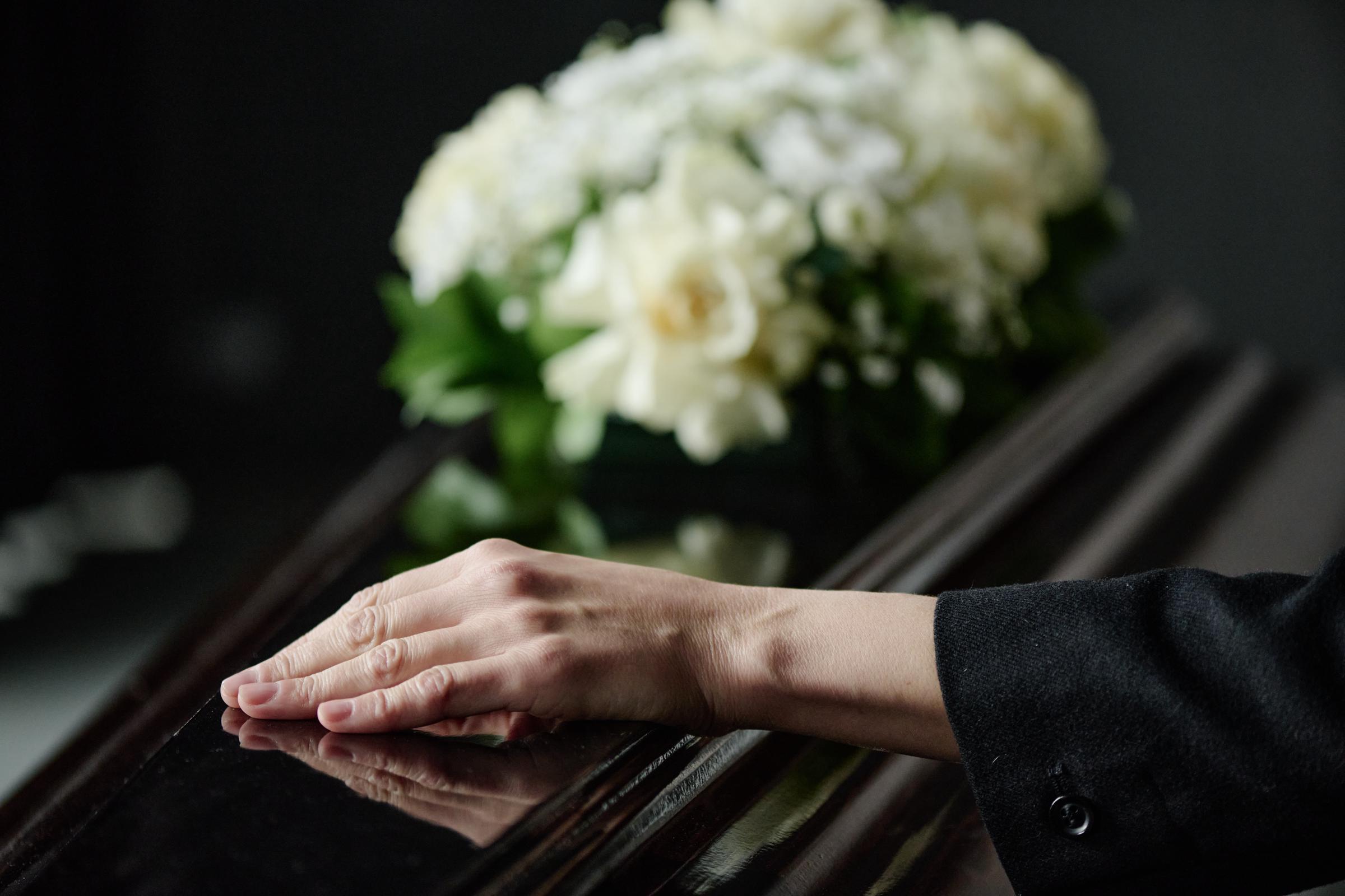 A woman's hand touching a coffin | Source: Shutterstock