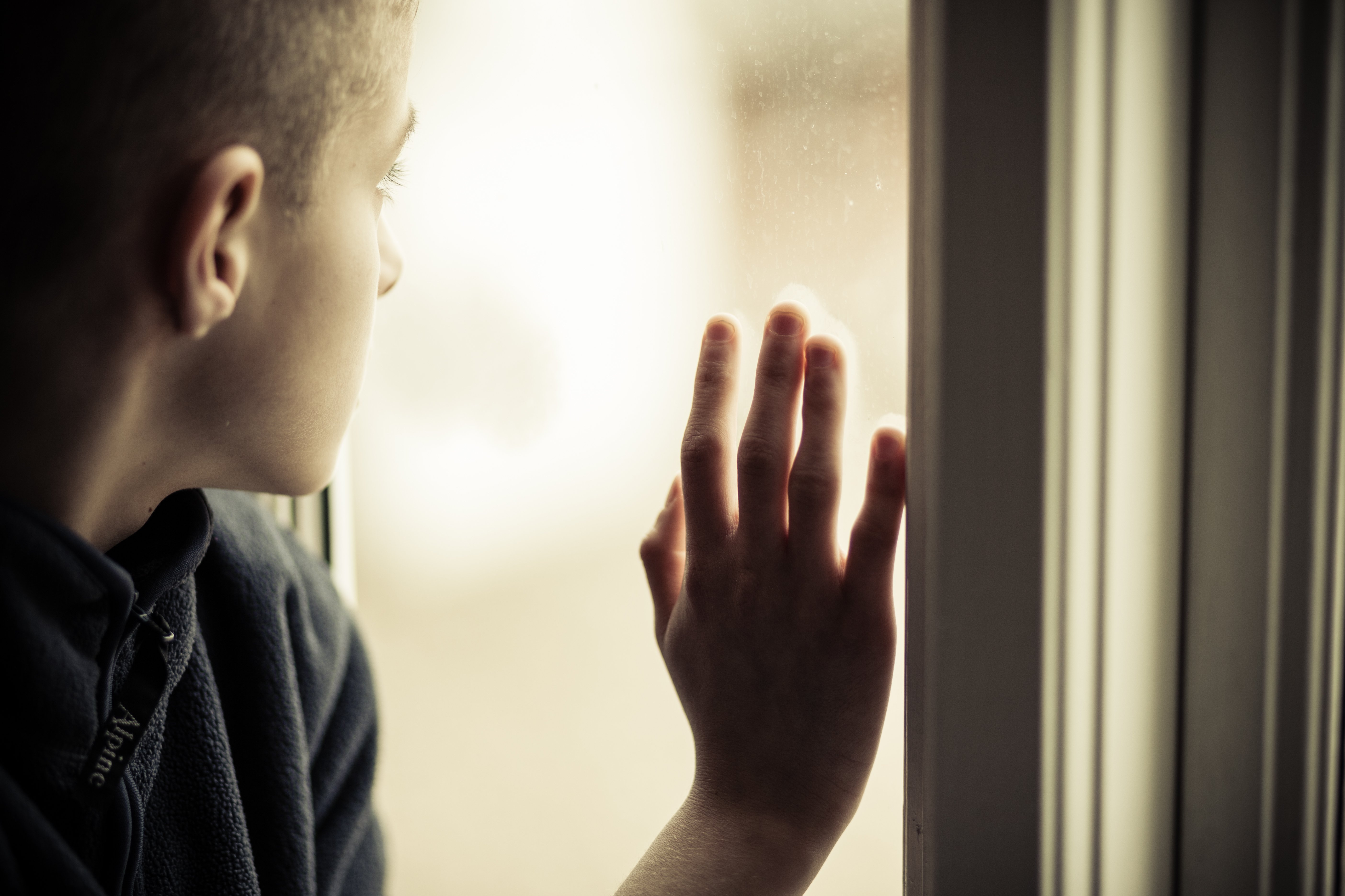 Lonely boy staring out of a window. │Source: Shutterstock
