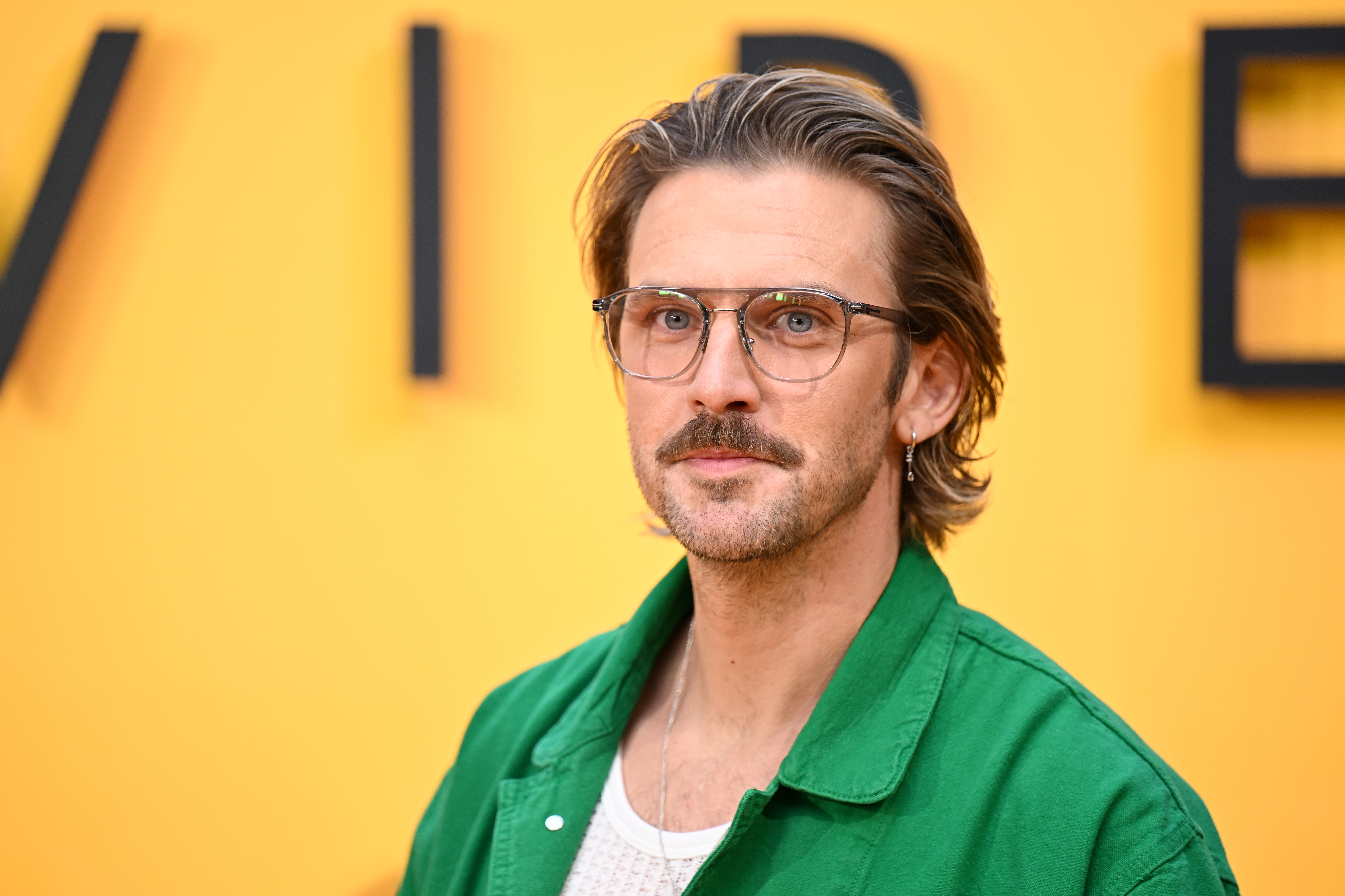 At the 2025 premiere of "Swiped," Stevens looked nearly unrecognizable with a bold, trend-forward style. Sporting longer hair, a moustache, glasses, and a single earring, he paired a casual green jacket with a white mesh shirt, showing just how far he's come in redefining his image since his early period drama days.