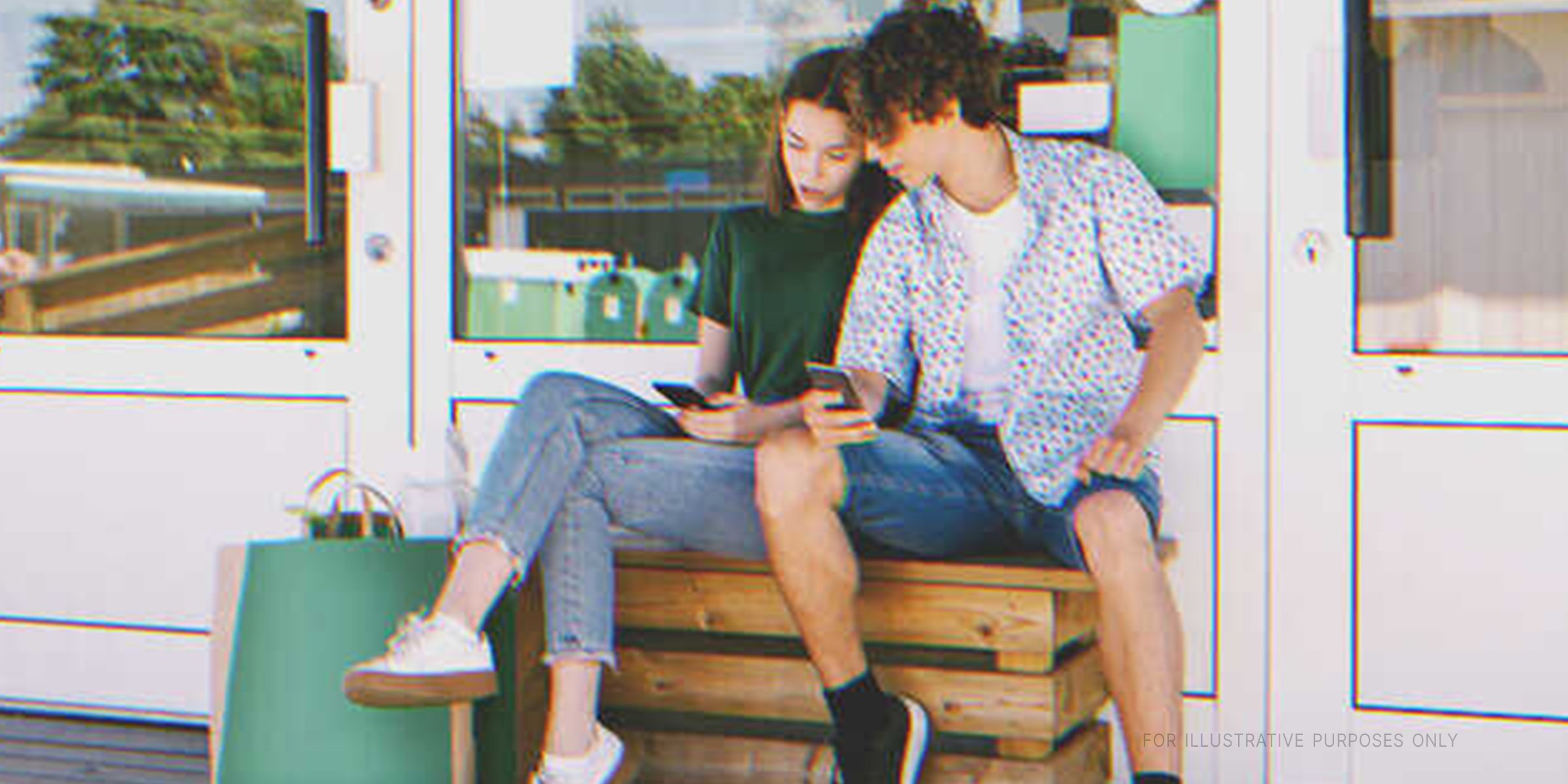 A boy and girl sitting outdoors and looking at a phone screen | Source: Shutterstock