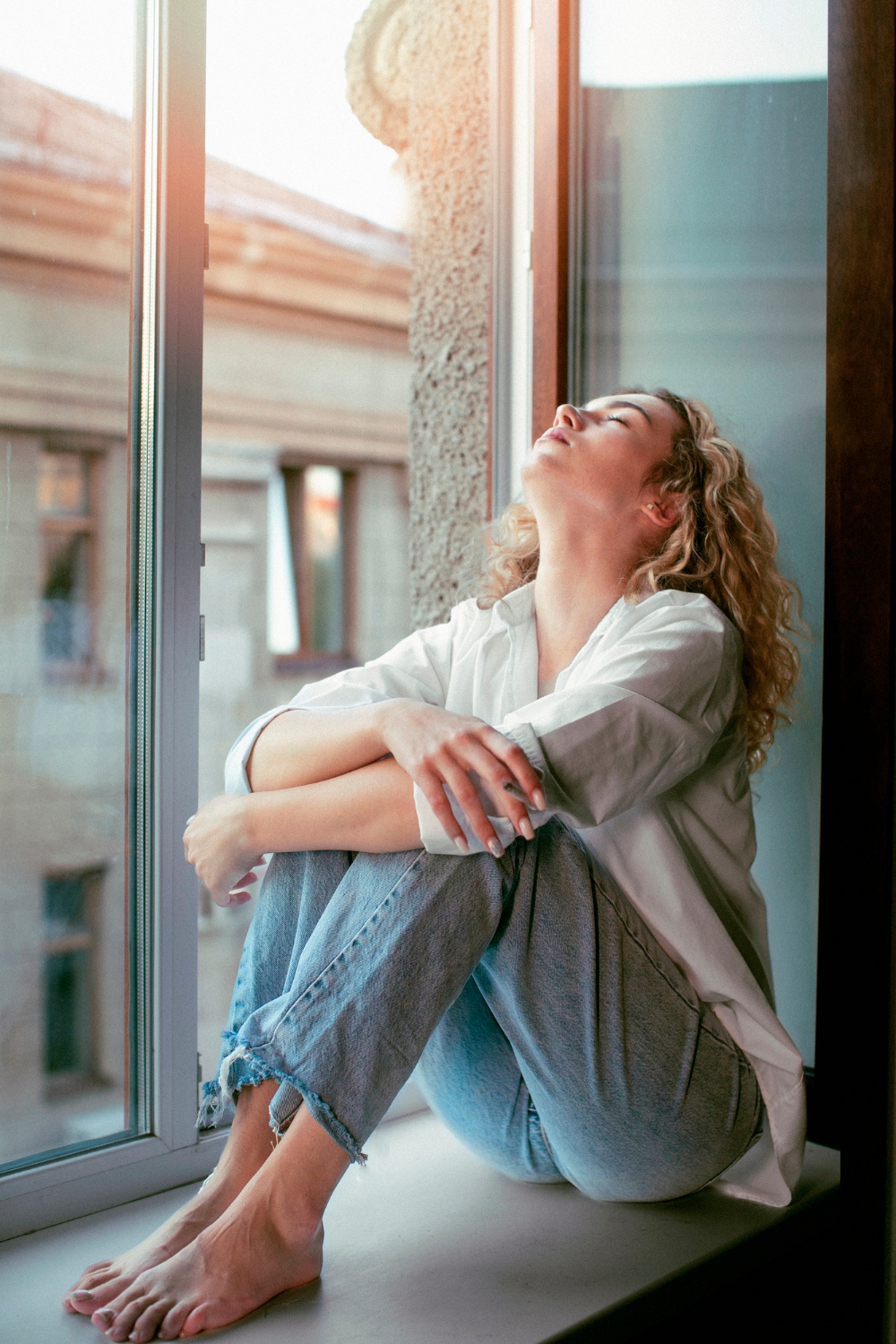 A sad woman sitting on a windowsill | Source: Freepik