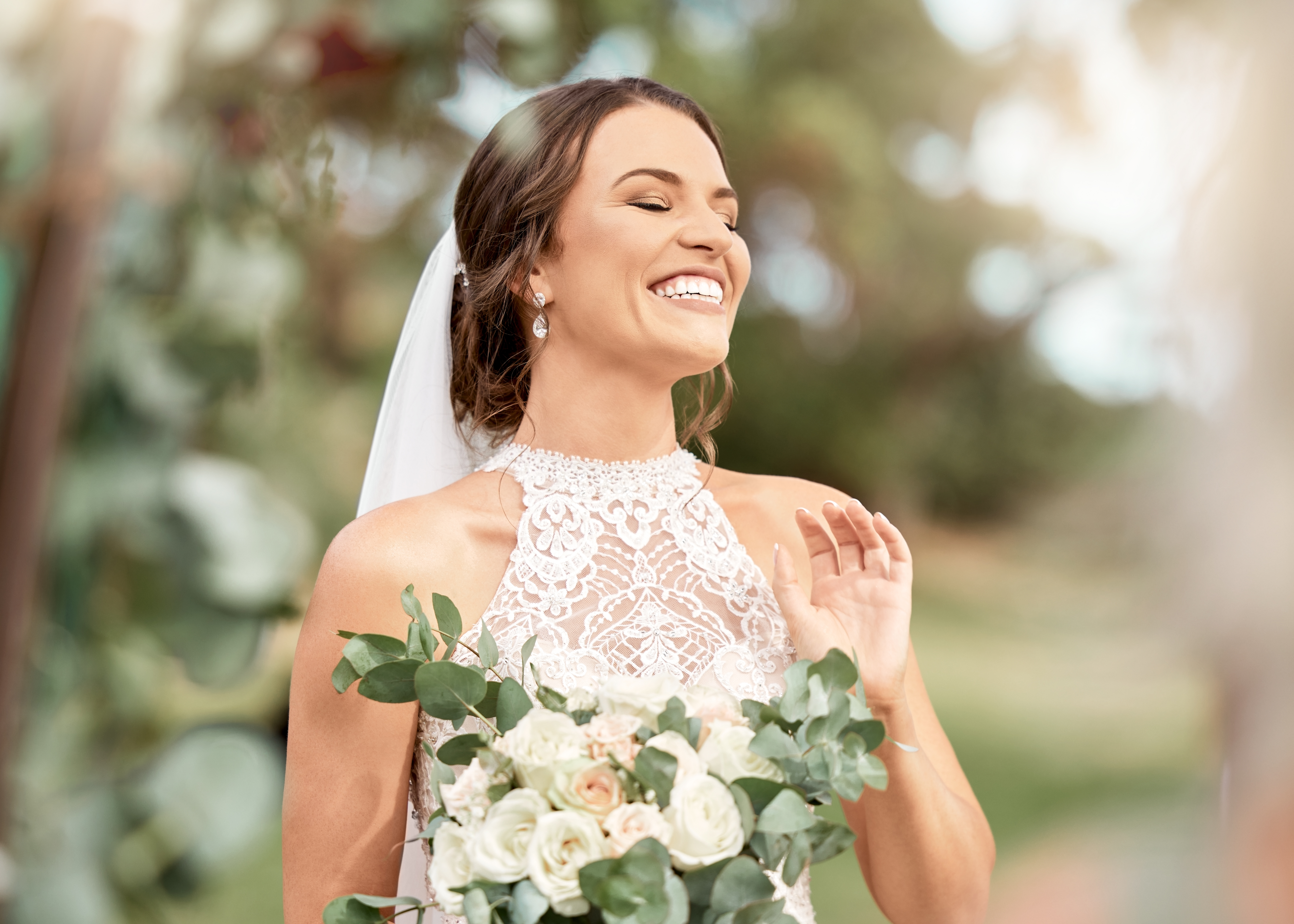 Excited bride in wedding with bouquet in nature park with green trees, bokeh and summer sunshine. Happiness, commitment and dream of a beauty woman with flowers for marriage in outdoor lens flare | Source: Getty Images
