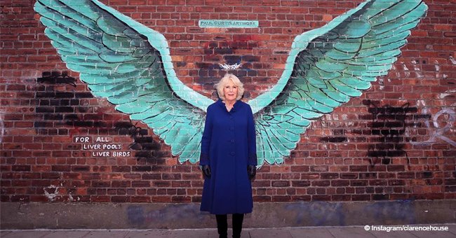 Camilla looks radiant posing in a bright blue coat and knee-high boots near Liver Bird wings