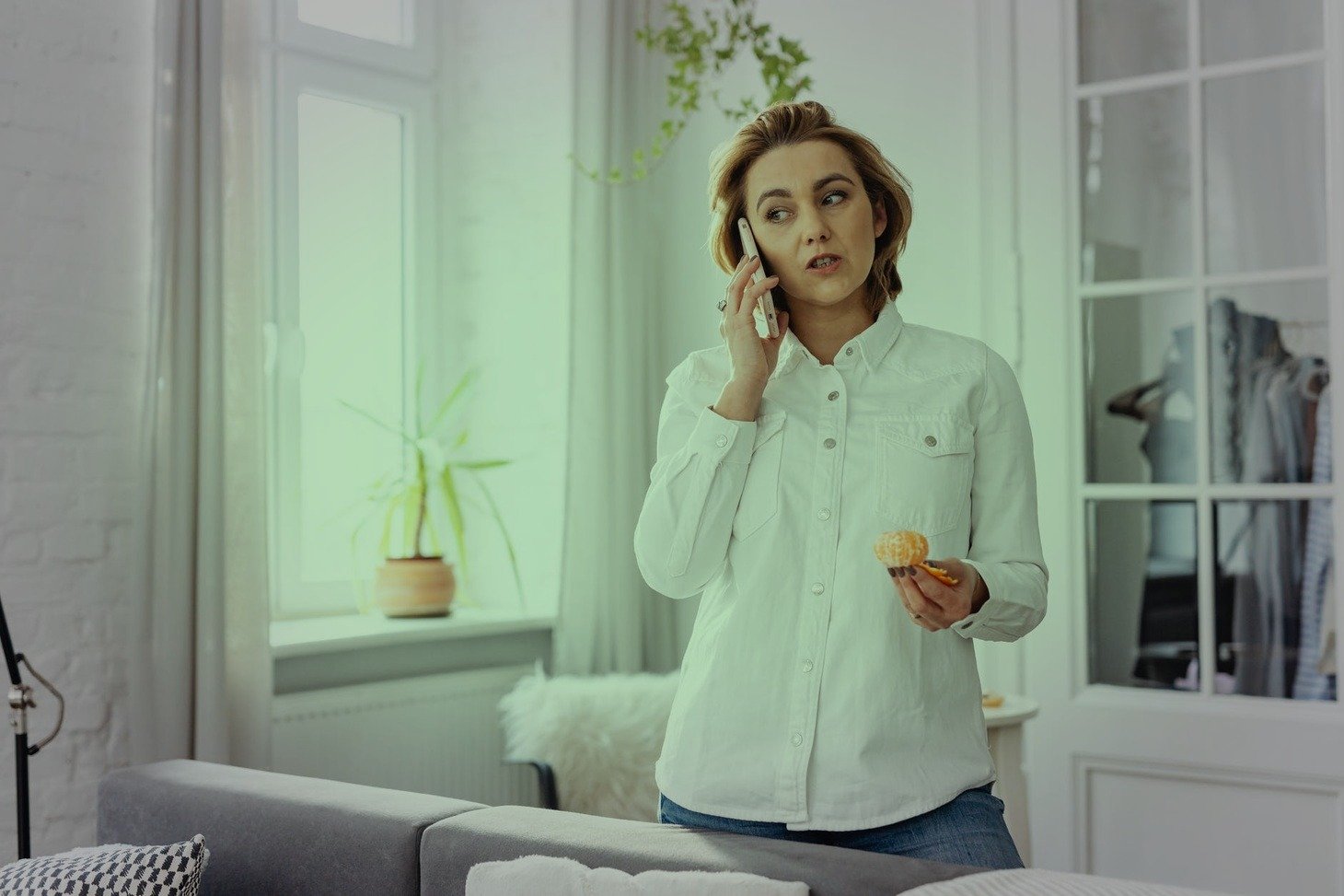 Mujer joven sostiene una conversación telefónica mientras come una fruta. | Foto: Pexels