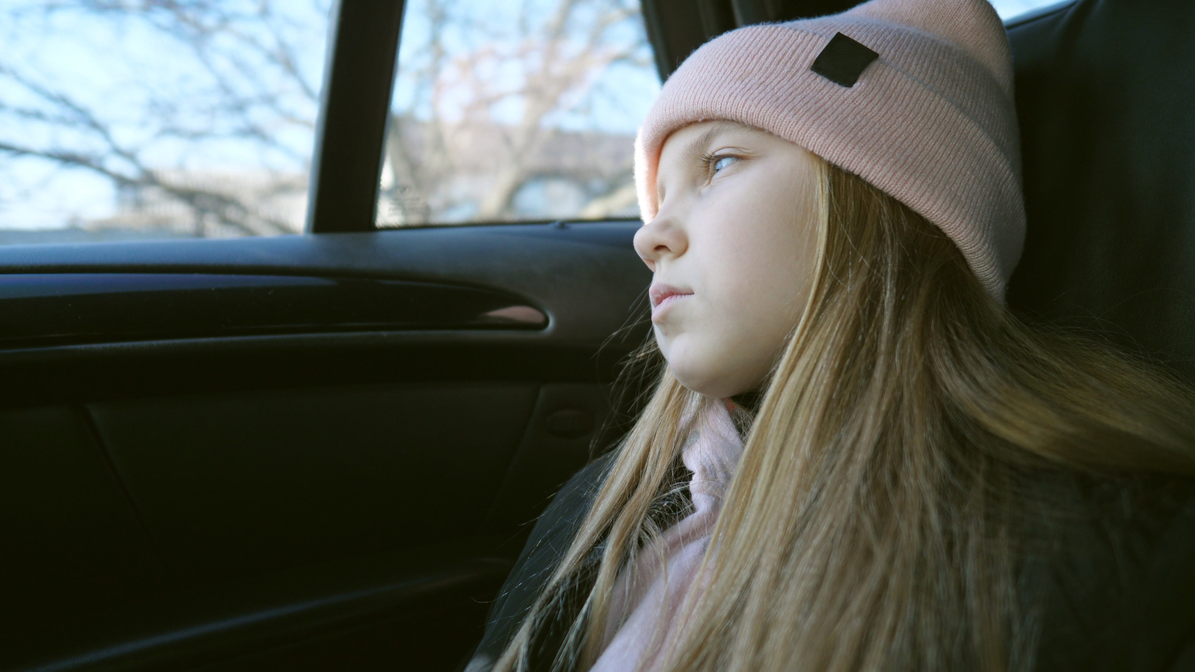 Beautiful female kid with long blonde hair looks outside through the window in the backseat of a moving car | Source: Shutterstock.com