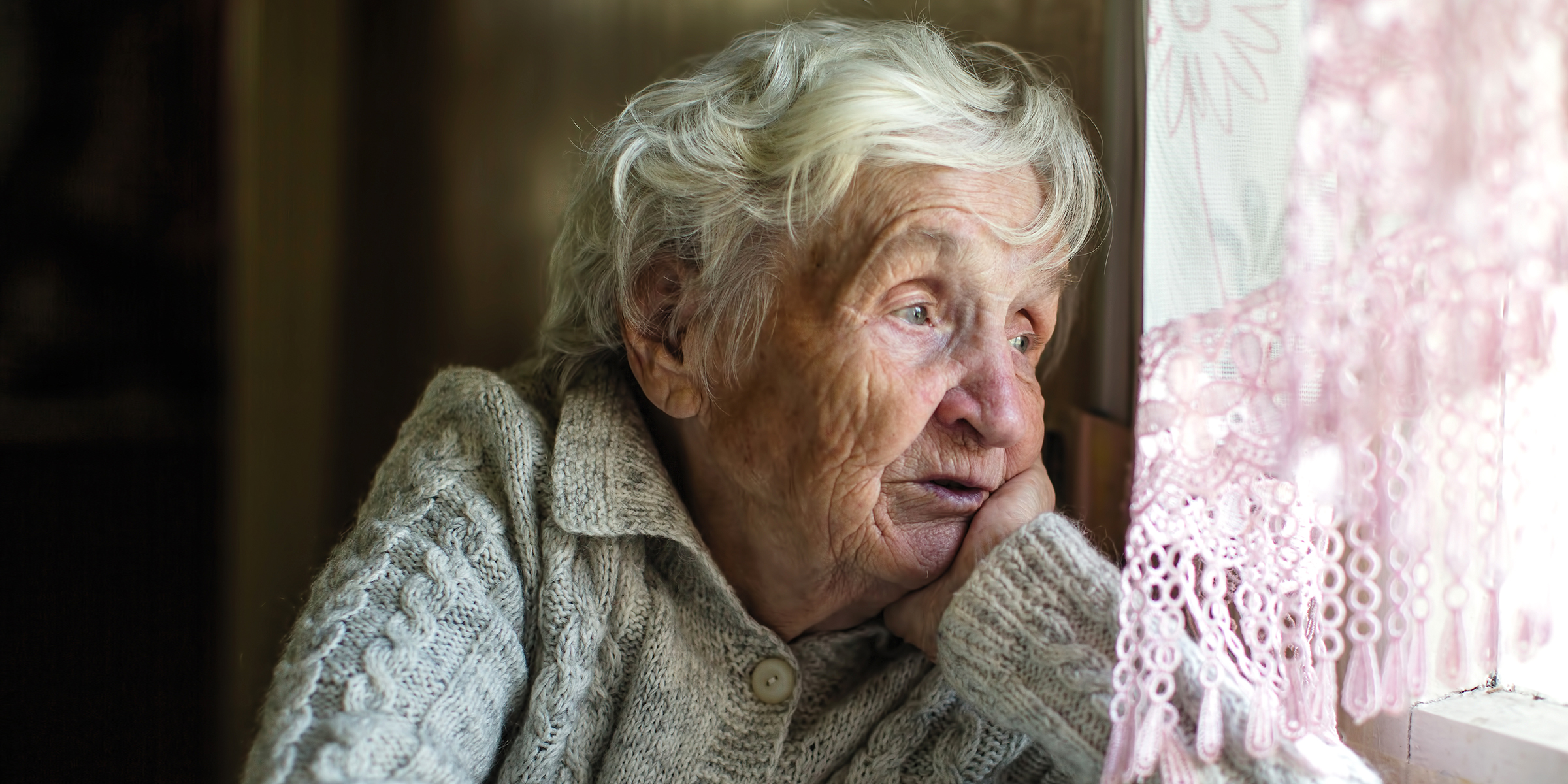 A sad elderly woman staring out a window | Source: Shutterstock