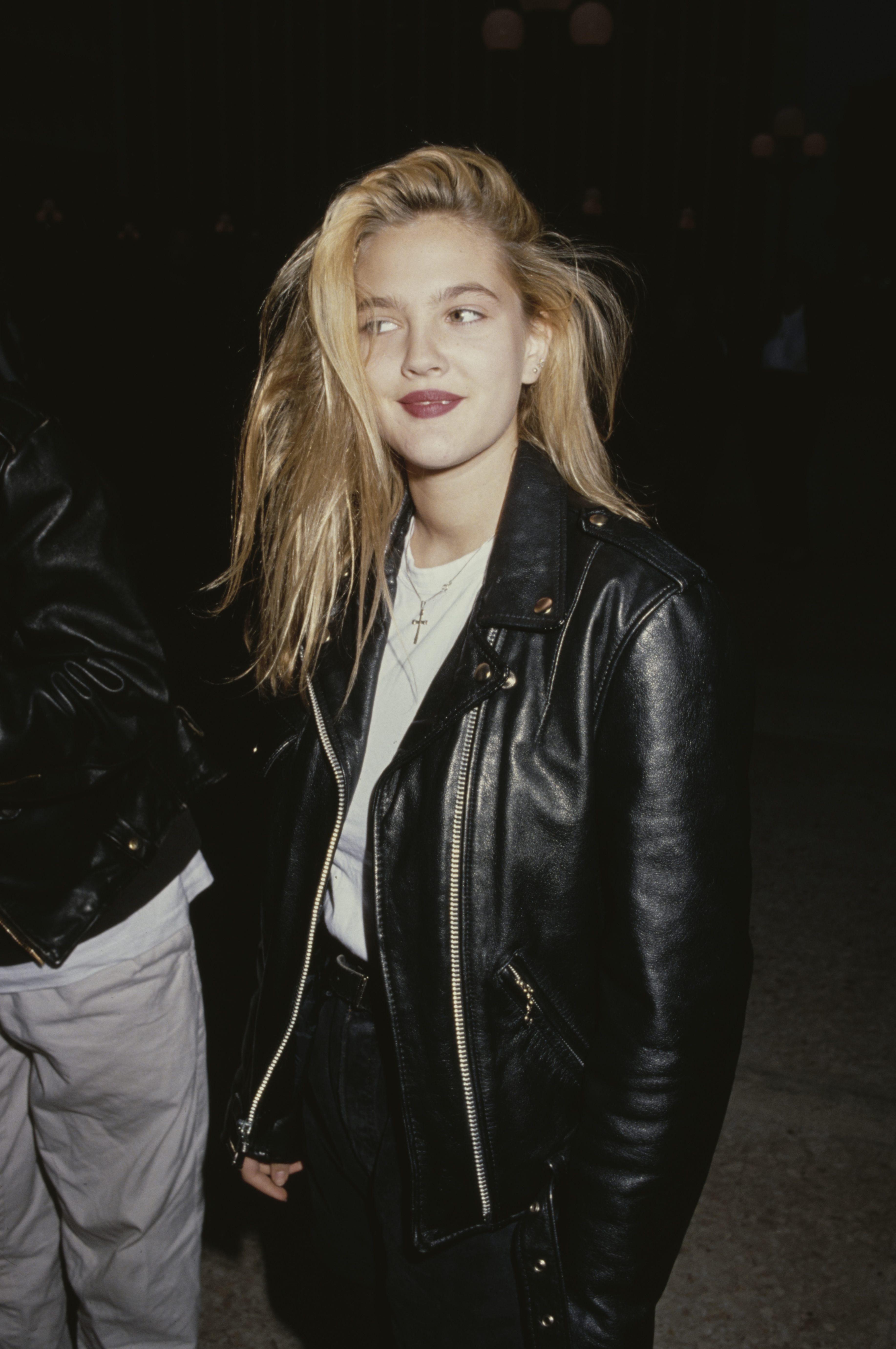 Drew Barrymore, wearing a white t-shirt beneath a black leather jacket, attends the Century City premiere of "Longtime Companion," held at Cineplex Odeon Century Plaza Theaters in California, circa 1990. | Source: Getty Images