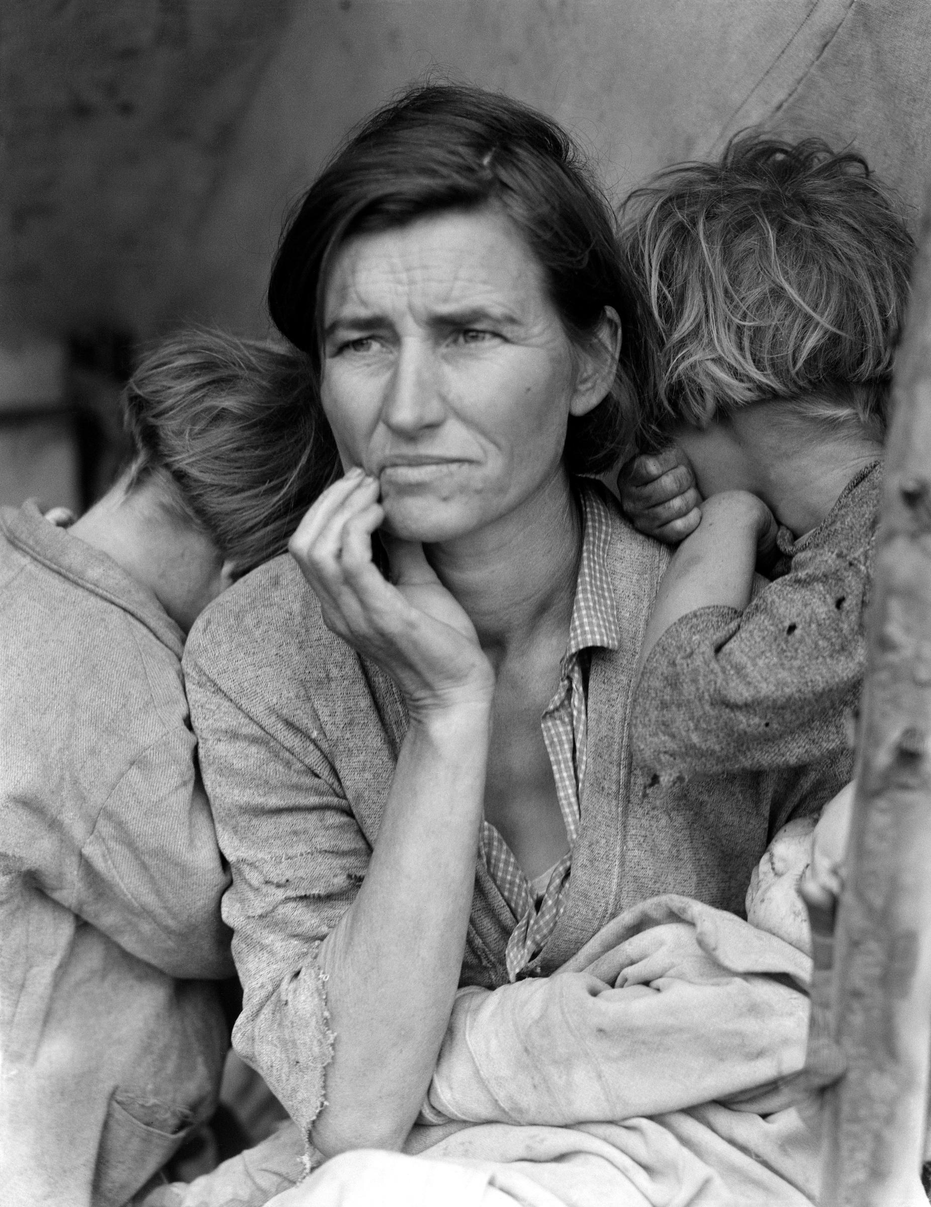 A destitute mother cradles her baby as two children cling to her shoulders in a migrant camp in Nipomo, California, circa 1936. | Source: Getty Images