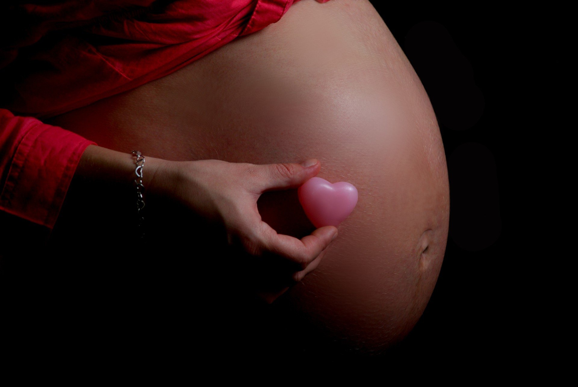 A person showing off an exposed pregnant baby bump while holding a little pink heart against it | Photo: Needpix