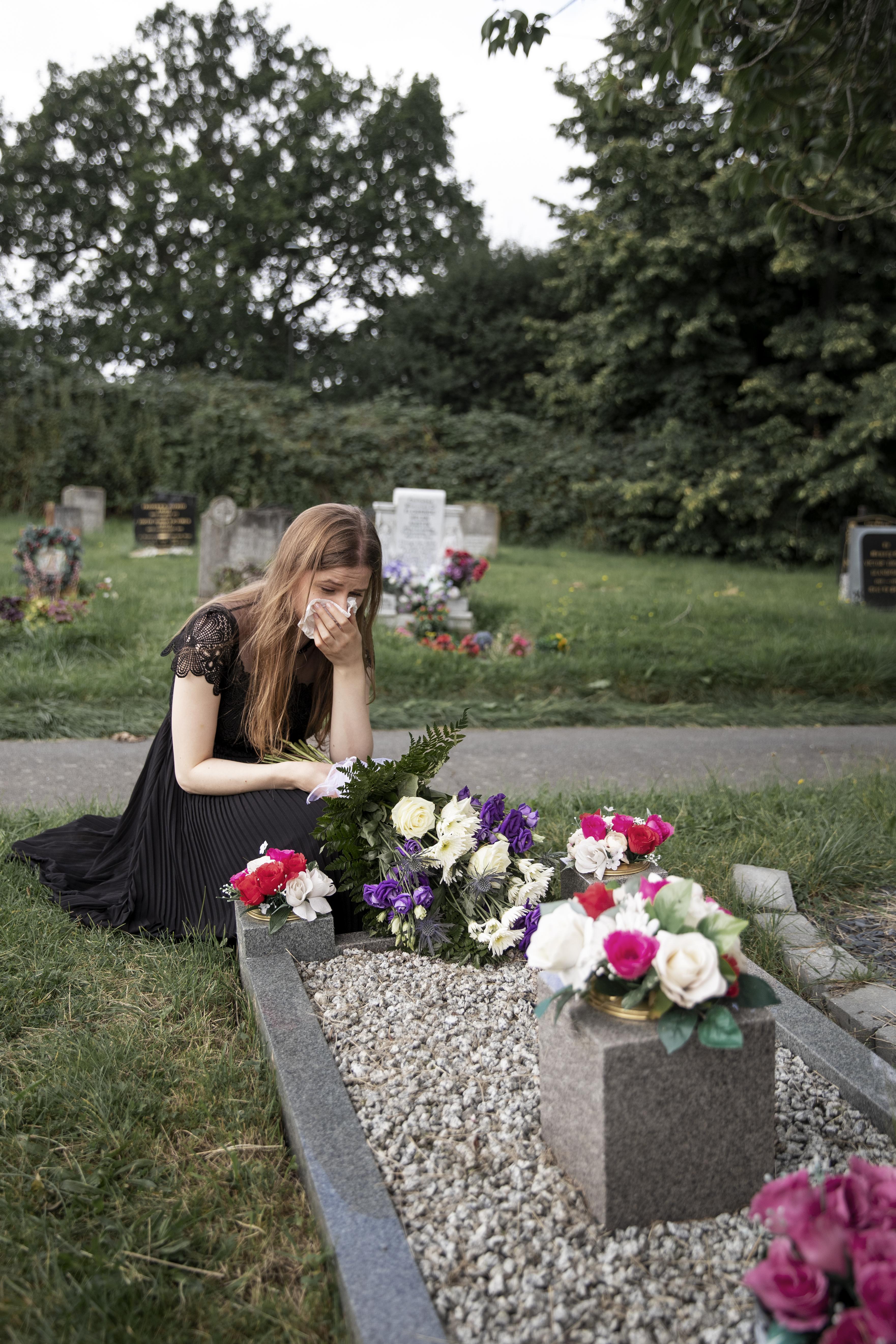 A grieving young woman in front of a grave in a cemetery | Source: Freepik