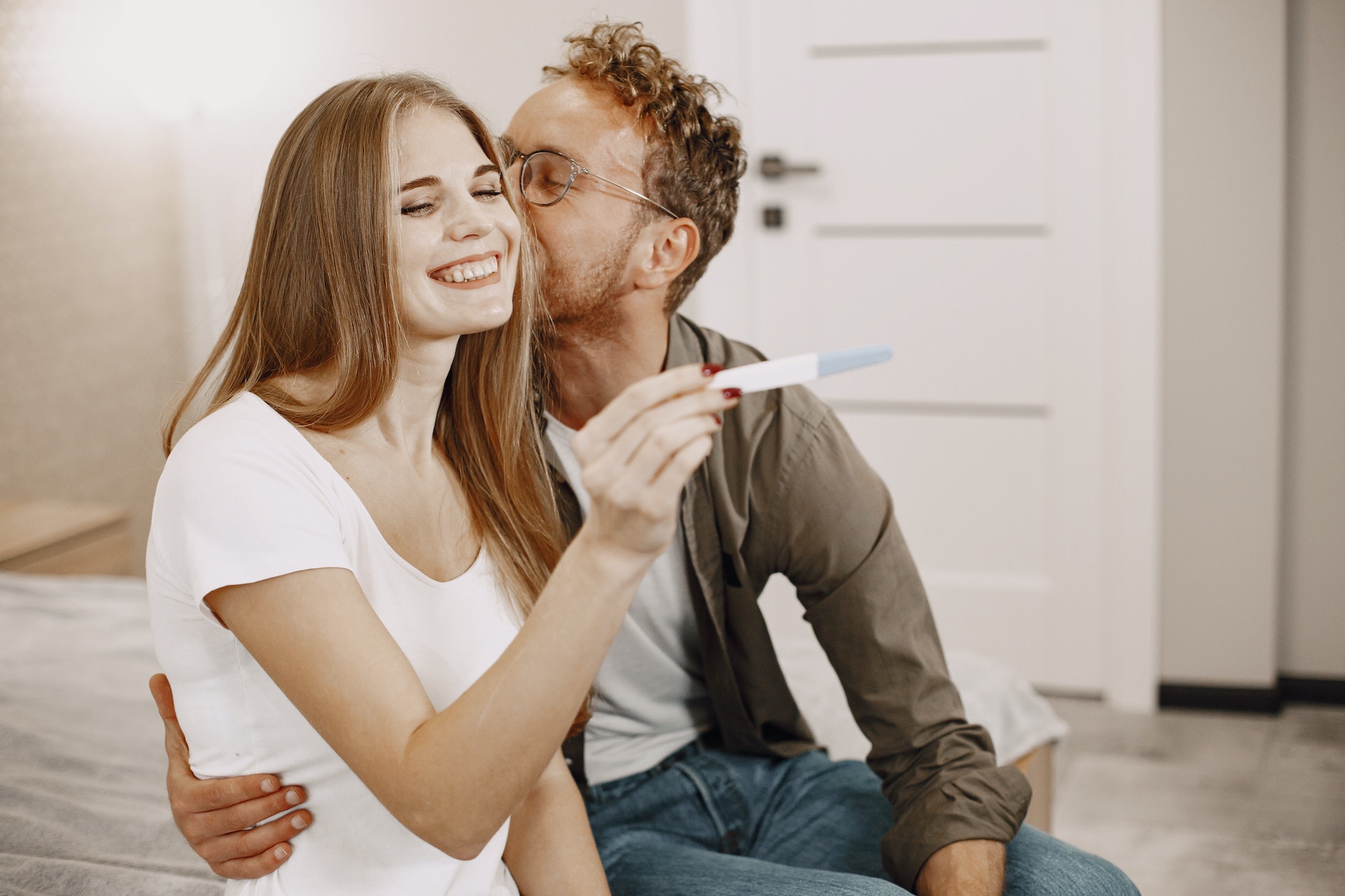 A woman holds a pregnancy testing kit while a man kisses her | Source: Pexels