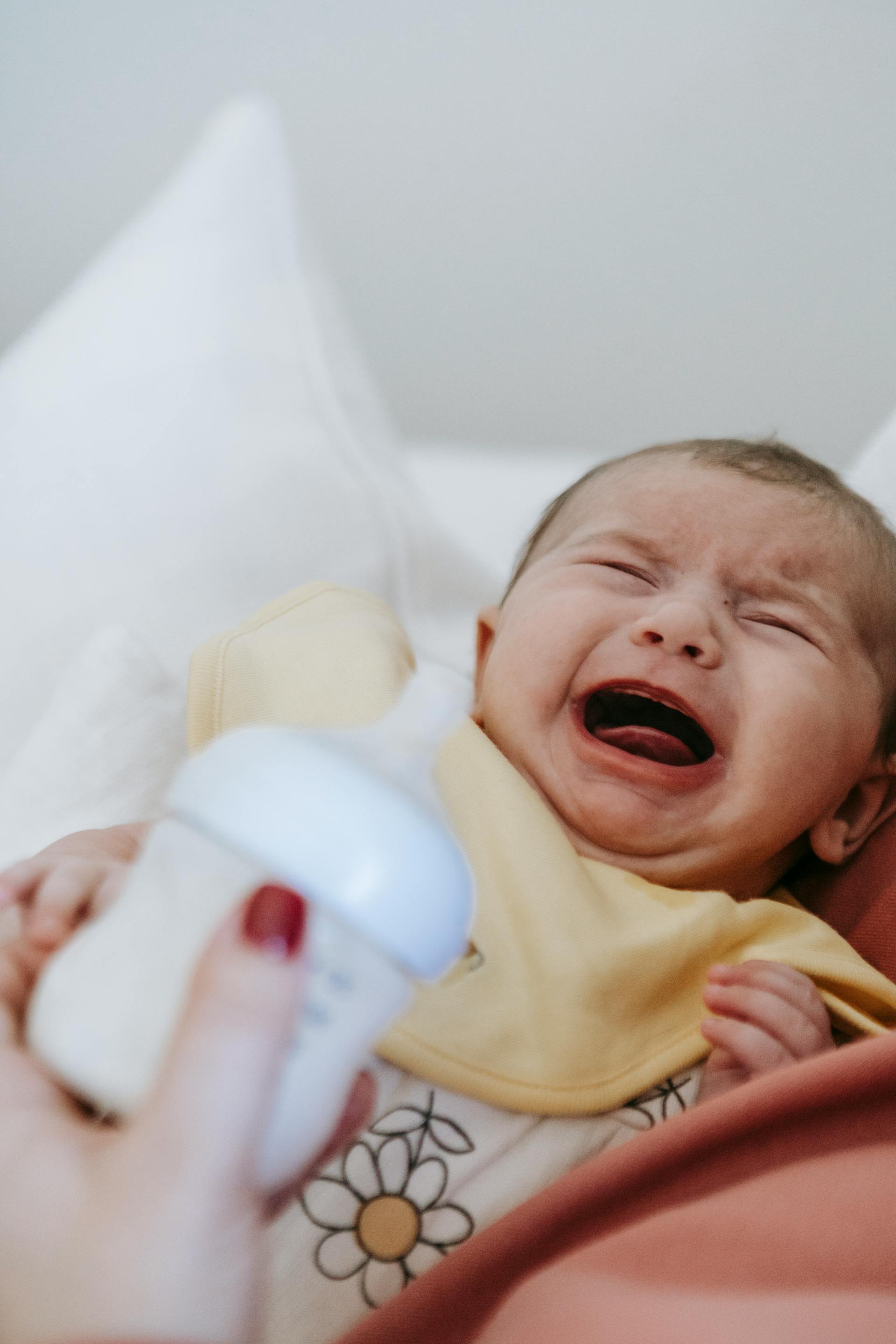 A woman holding a crying baby and a feeding bottle | Source: Pexels