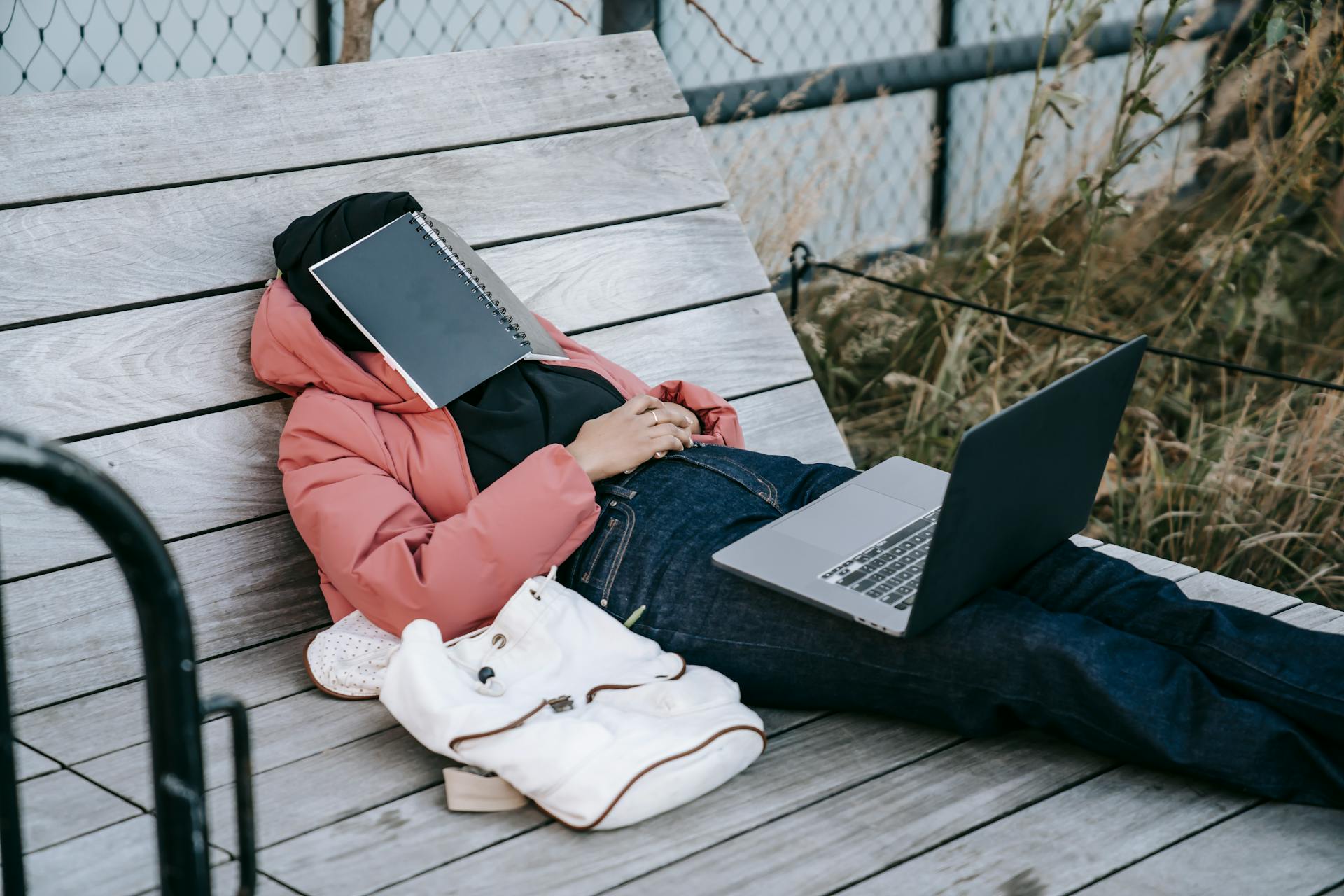 An unrecognizable woman with an open laptop resting on a bench with a book on her face | Source: Pexels