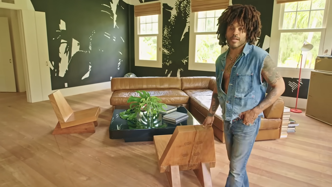 Lenny stands next to sculptural wooden lounge chairs designed by Zanine Caldas, beautifully showcasing his love for classic Brazilian design. | Source: YouTube/@Archdigest