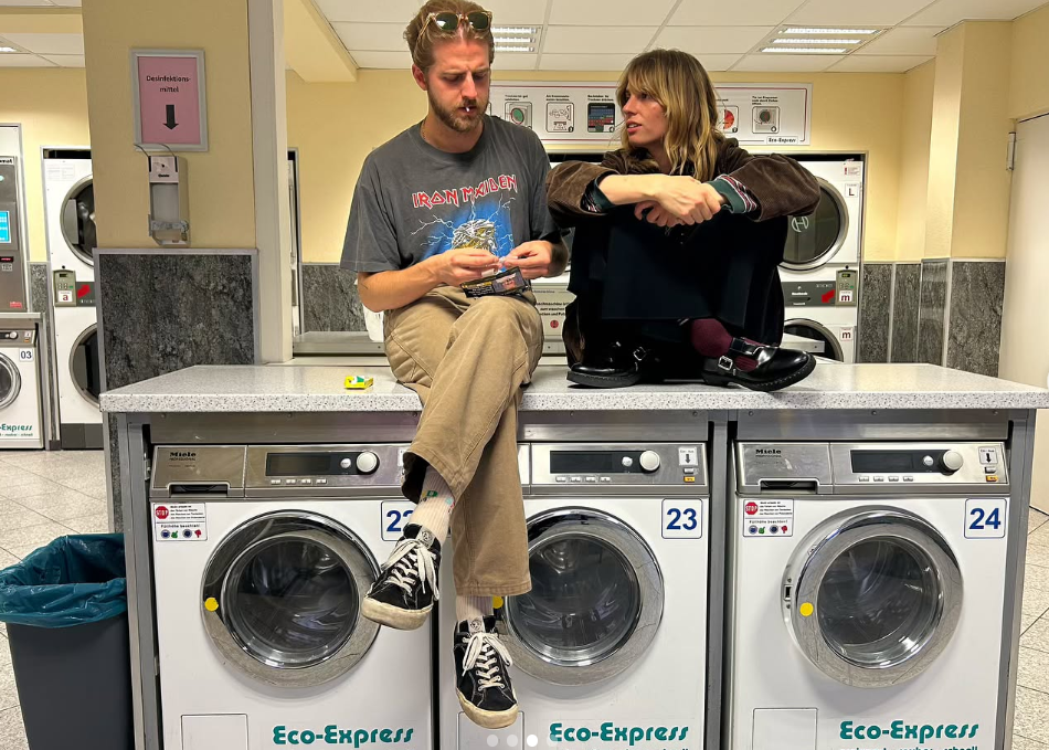 The pair, Maya Hawke and Christian Hutson, sit atop laundromat washing machines, mid-conversation, dressed in relaxed, everyday clothes. | Source: Instagram/maya_hawke