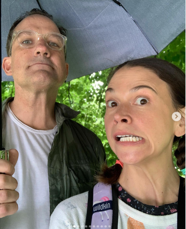 Sutton Foster poses beside Ted Griffin under an umbrella, pulling a playful expression during a rainy outdoor moment. | Source: Instagram/suttonlenore