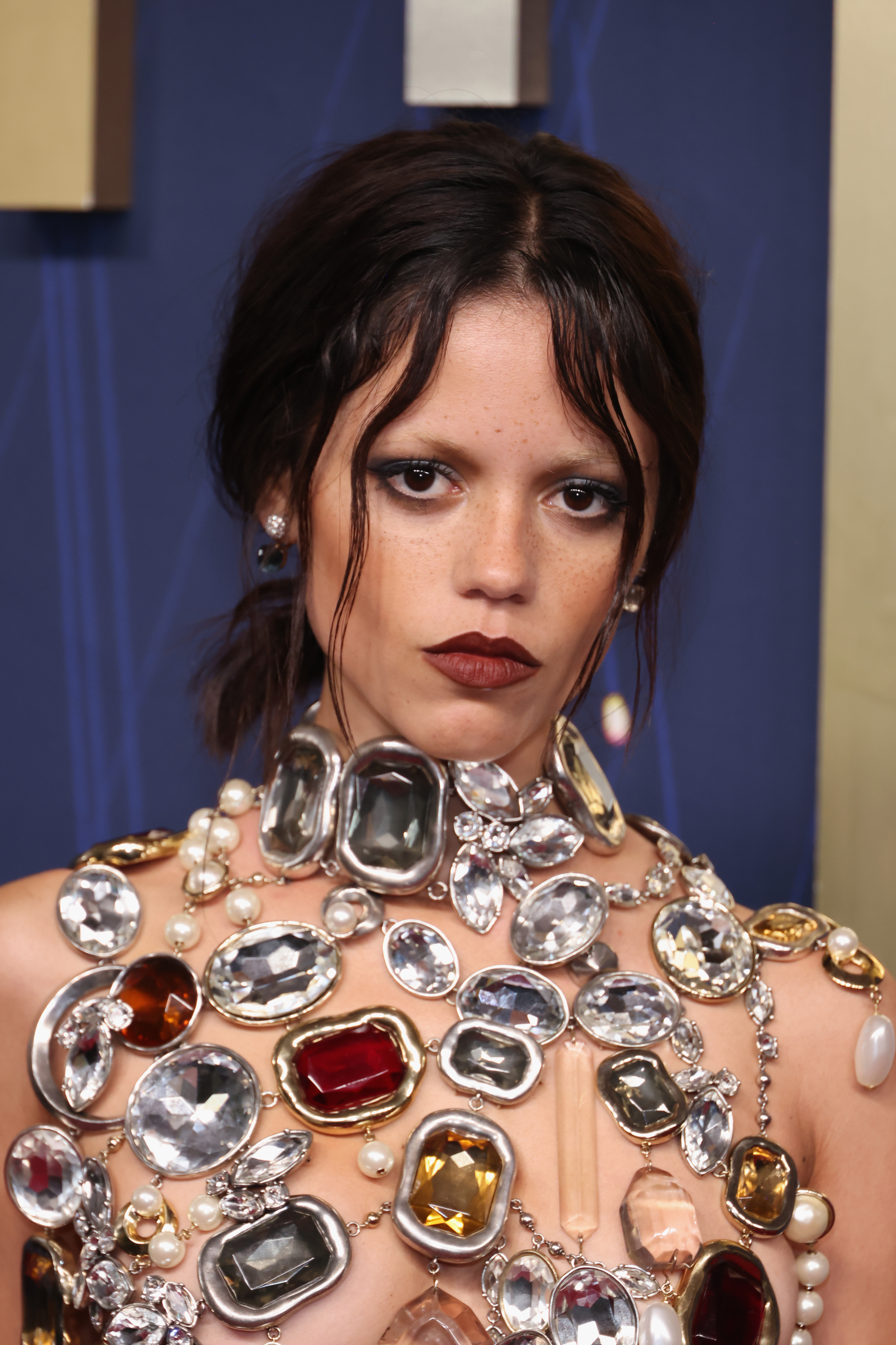 A closer shot showcases the top on Jenna Ortega that has stunned fans. It’s a shimmering bra-like design made of strands of pearls and gemstones in shades of gray, silver, and yellow, all glowing under the light.