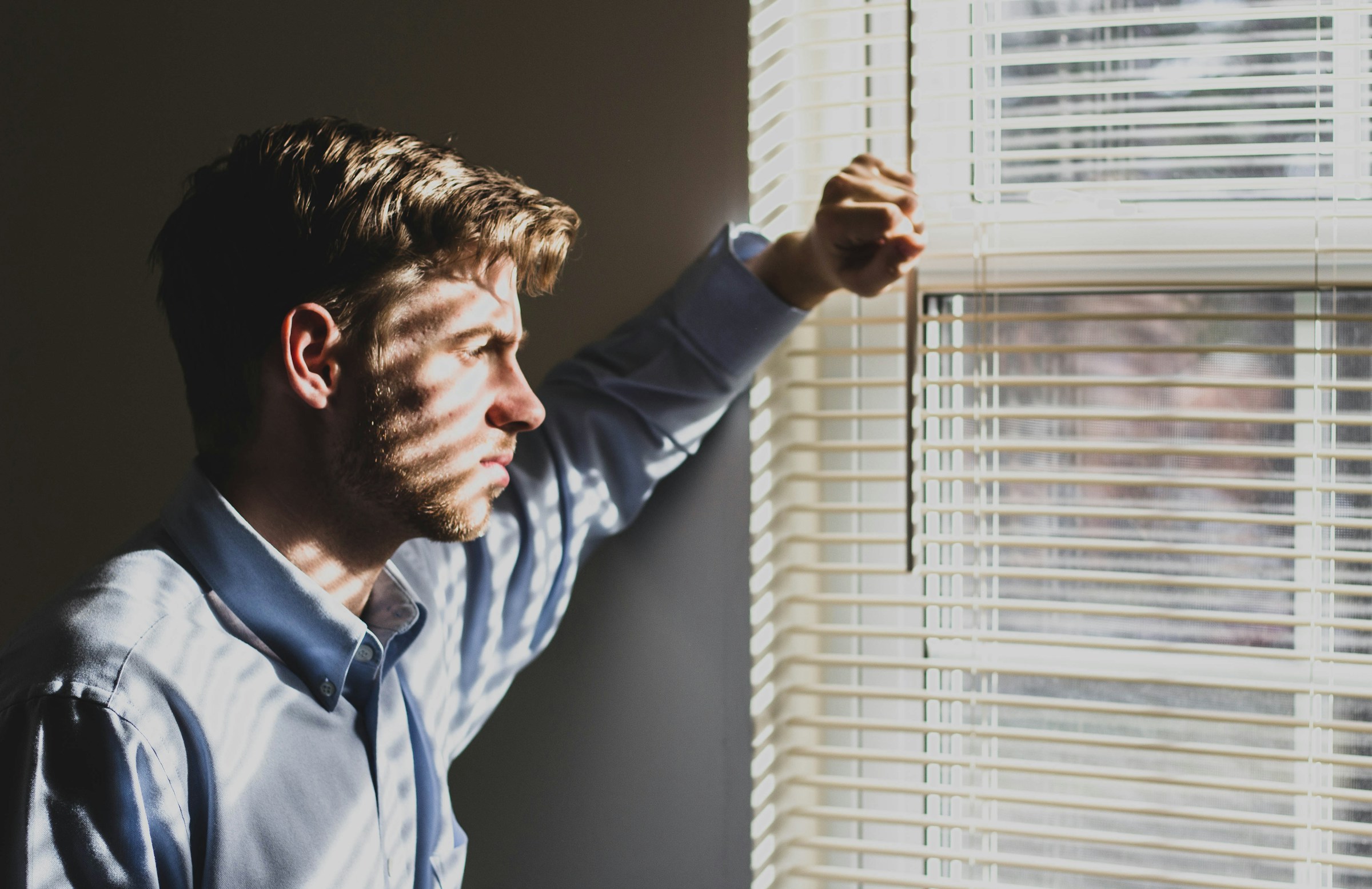 A pensive man looking through the window blinds | Source: Unsplash