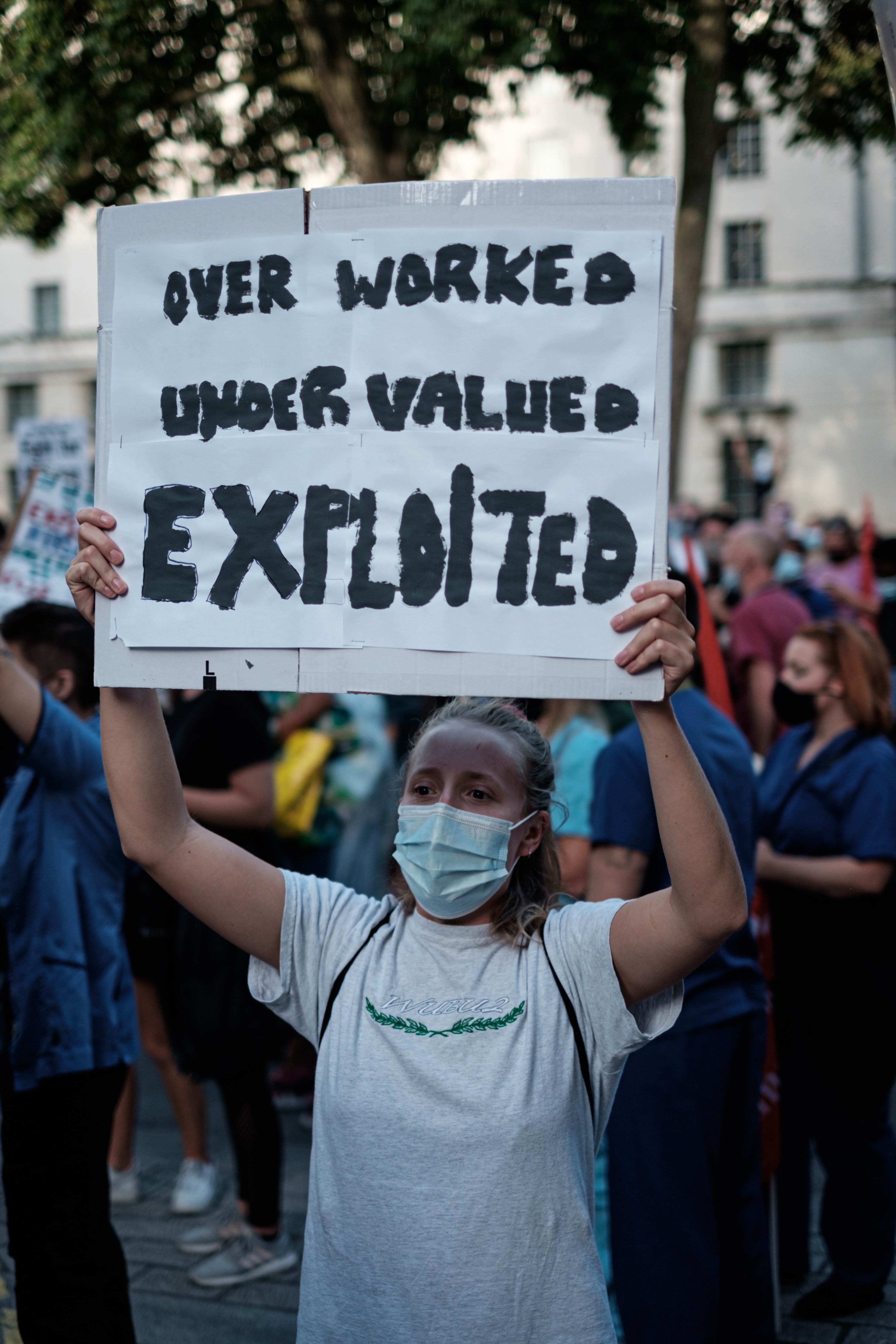 A protestor stands in the street holding up a poster that states "Over Worked, Under Valued, Exploited" | Photo: Unsplash/Ehimetalor Akhere Unuabona 