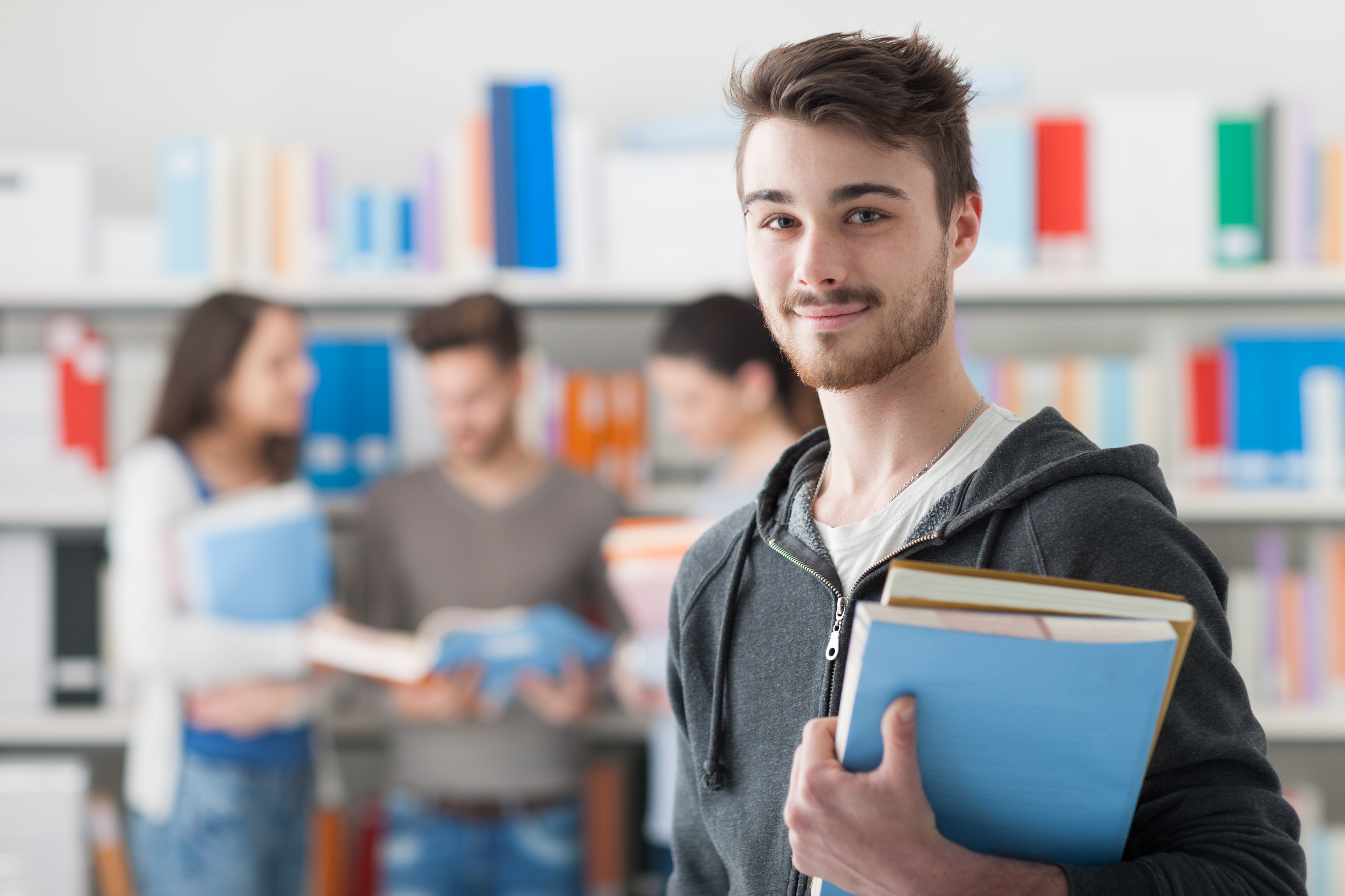 Estudiante sosteniendo libros y sonriendo a la cámara. Fuente: Shutterstock Estudiante sosteniendo libros y sonriendo a la cámara. Fuente: Shutterstock