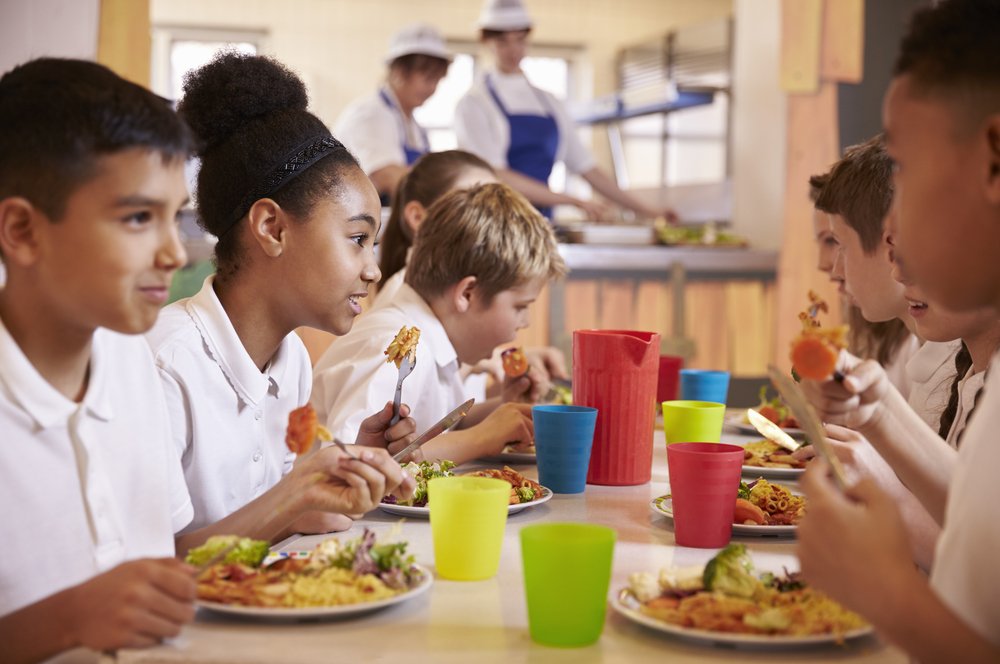 Niños de primaria almozando en la cafetería de la escuela. | Fuente: Shutterstock. Niños de primaria almozando en la cafetería de la escuela. | Fuente: Shutterstock.