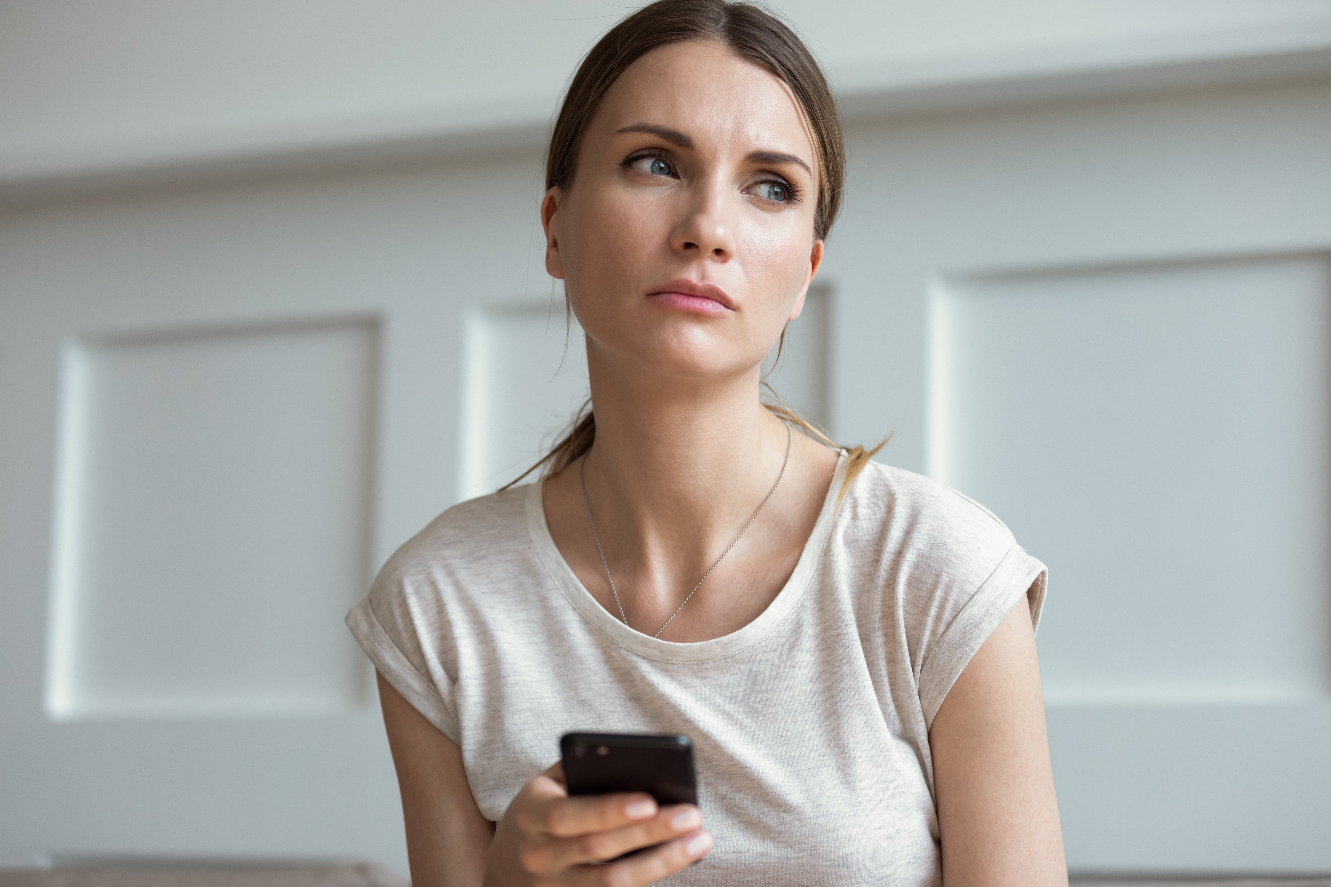 A woman holding a phone while looking thoughtful | Source: Shutterstock