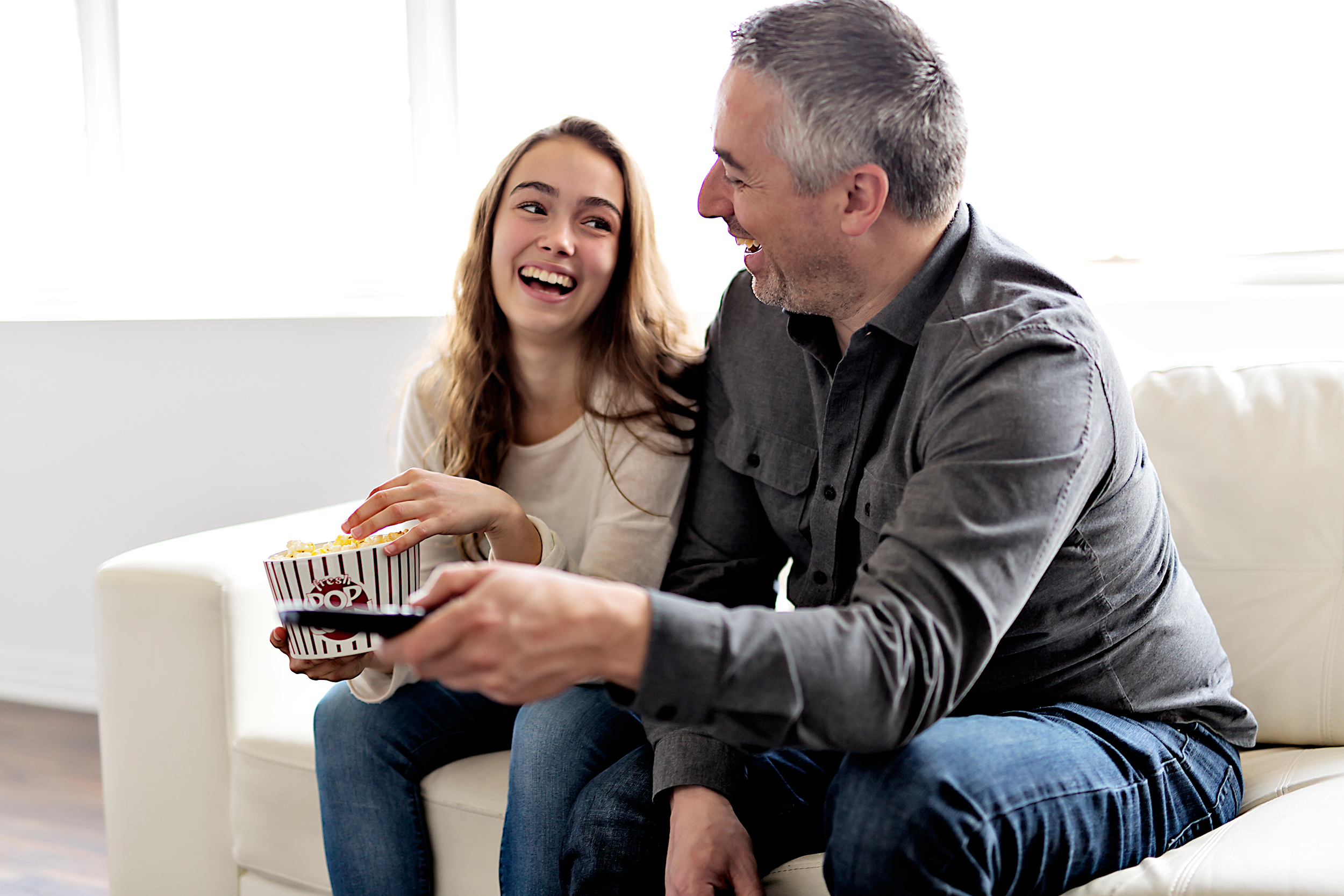 A daddy-daughter duo are pictured laughing together while watching TV and eating popcorn | Source: Shutterstock
