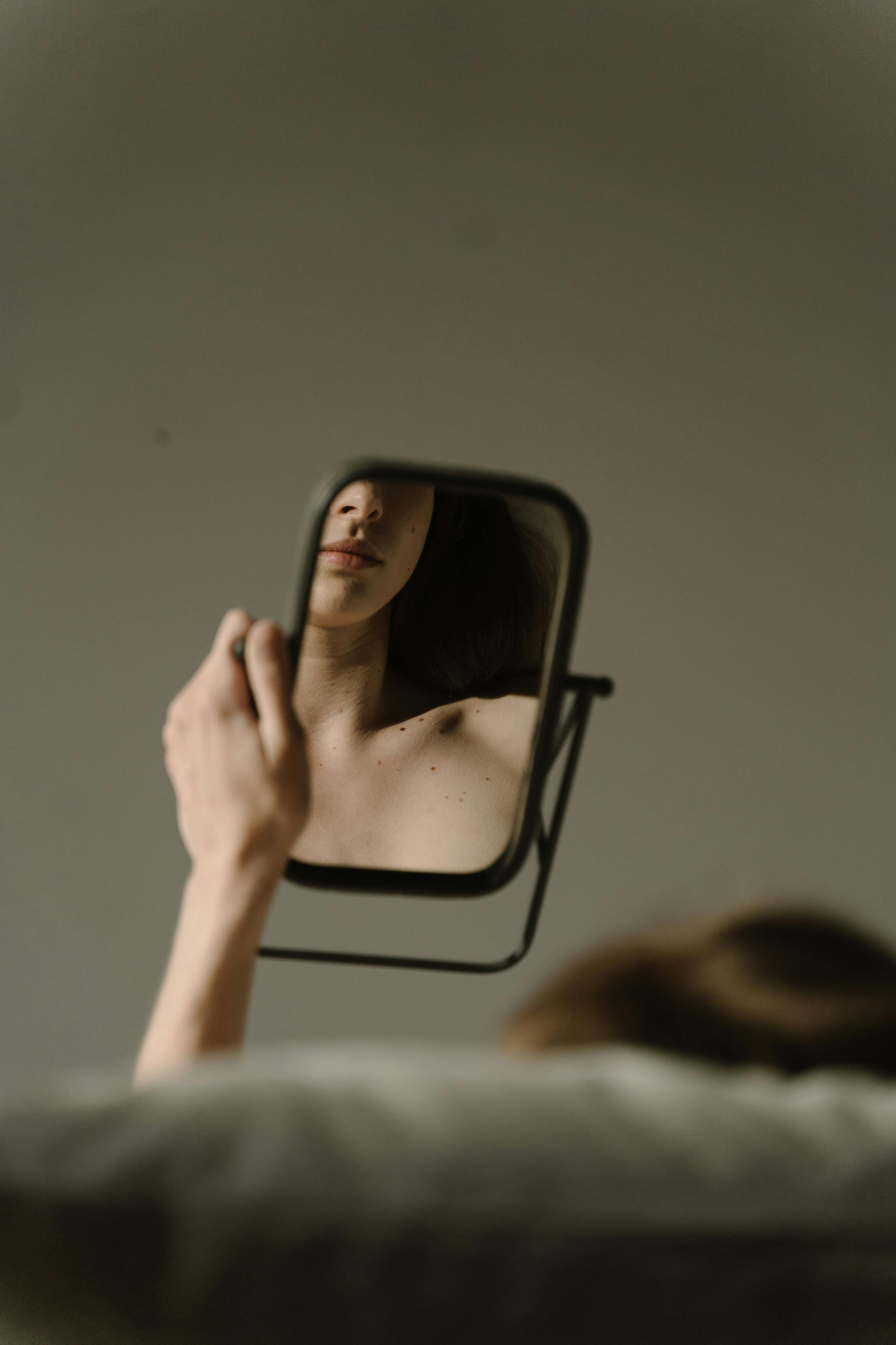 Woman sitting on a sofa looking at her reflection on a mirror | Source: Pexels
