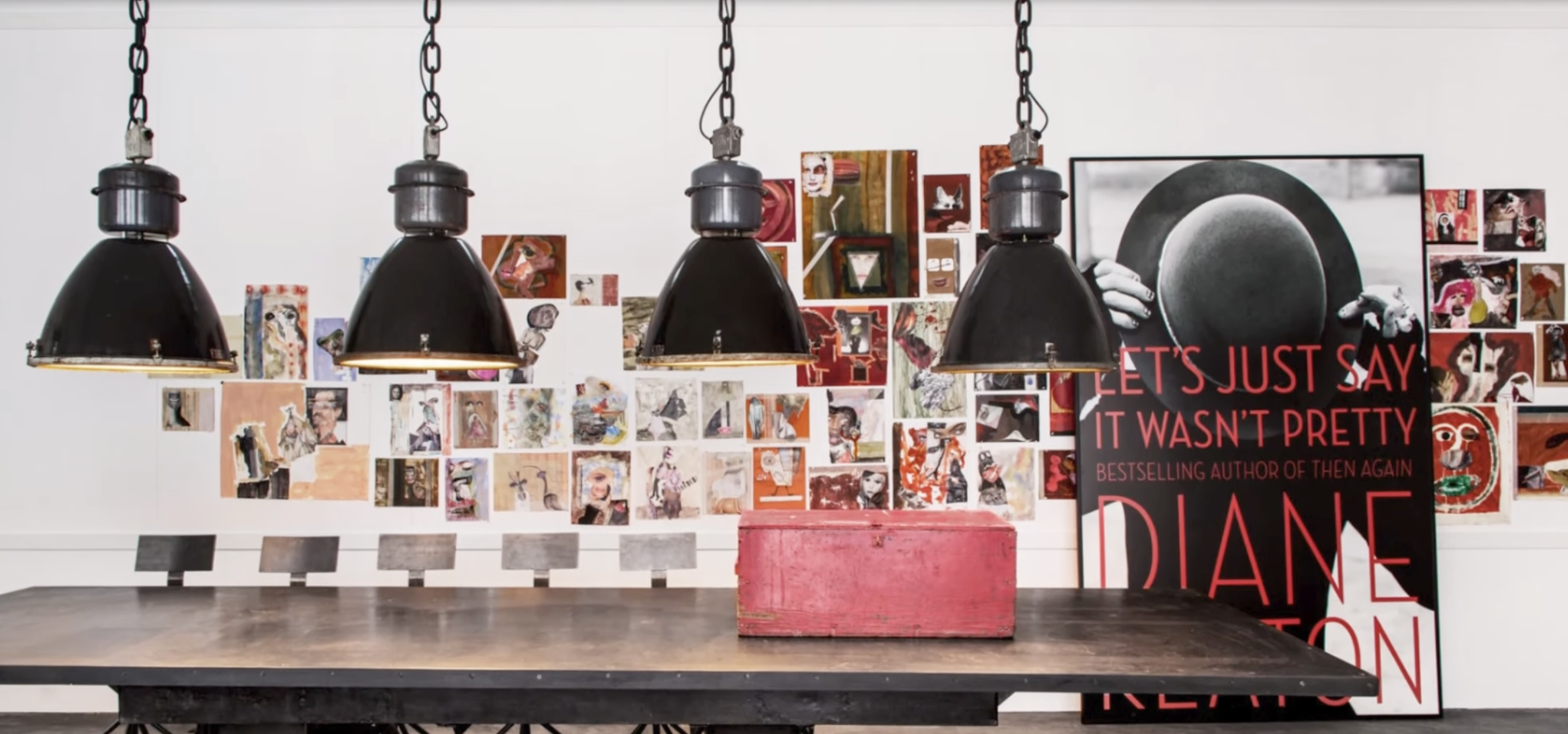 Art wall and industrial pendant lighting above a long table inside Diane Keaton’s Sullivan Canyon home, with a poster of her book “Let’s Just Say It Wasn’t Pretty” visible, dated February 3, 2022 | Source: YouTube/@FamousEntertainment500k