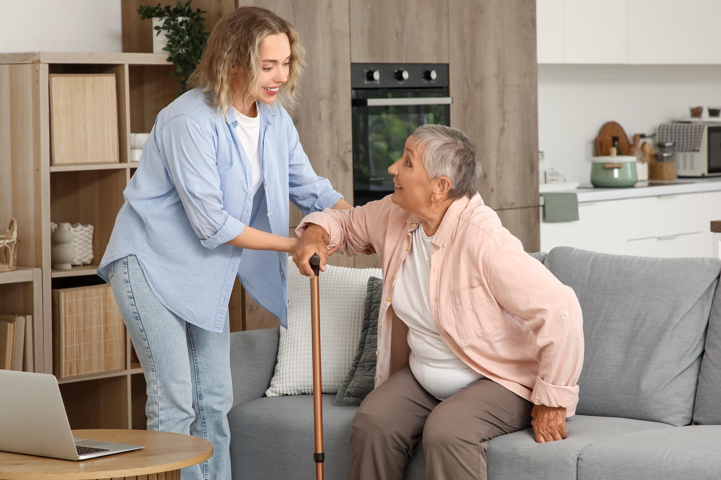 Young woman assisting an older woman as she gets up from a couch with a cane | Source: Shutterstock