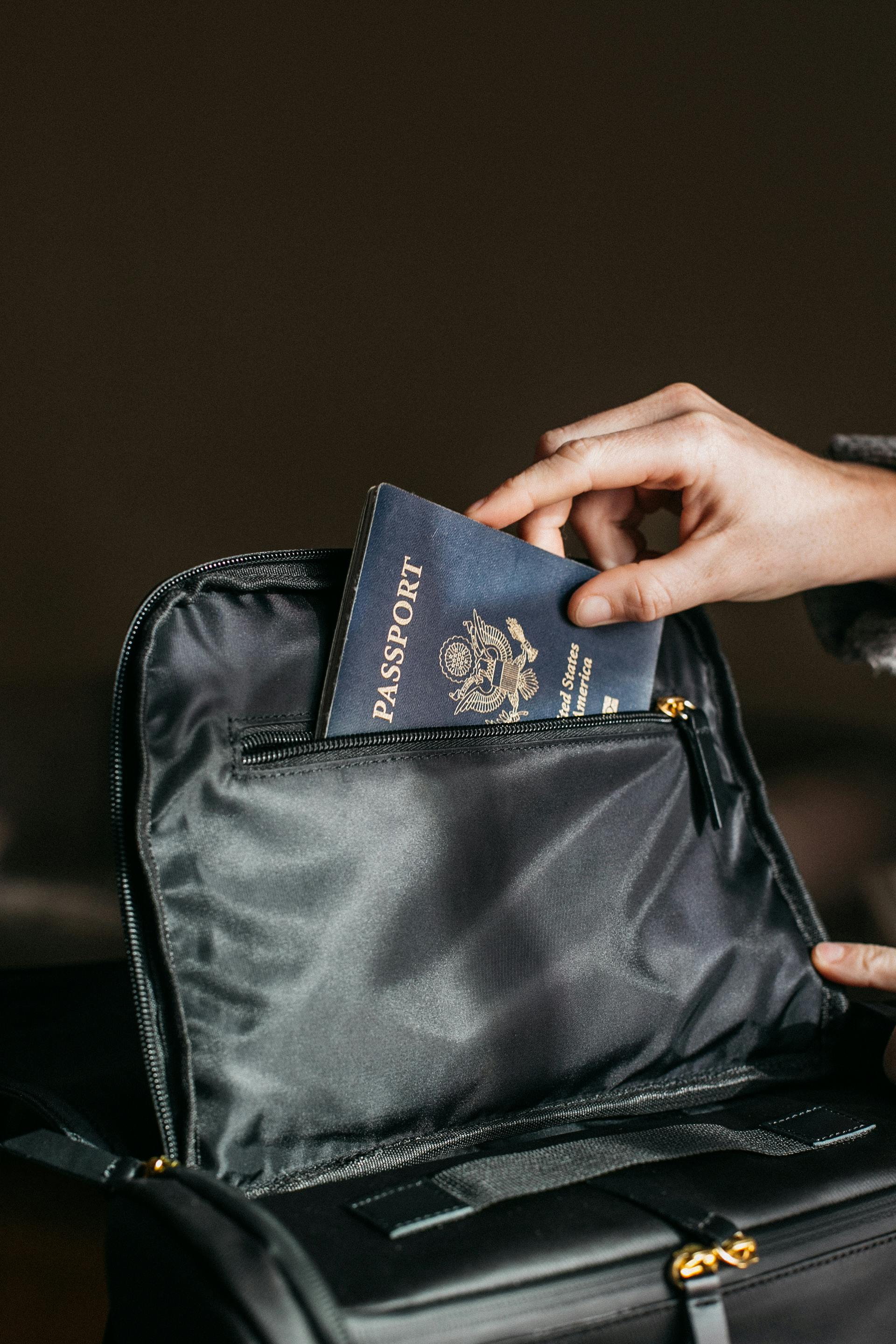 A closeup of a person putting a passport in a black bag | Source: Pexels