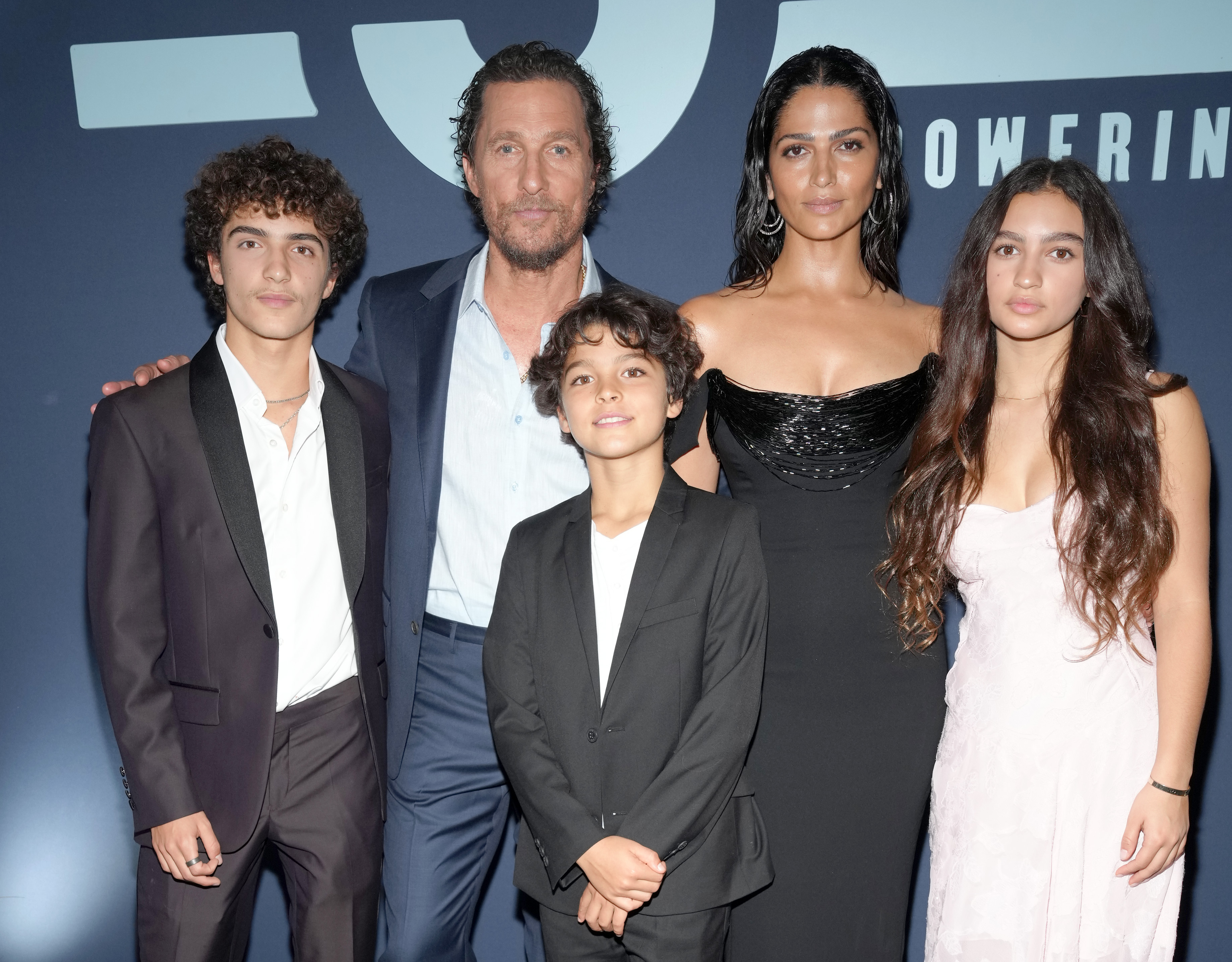 Levi, Livingston, and Vida McConaughey stand together in coordinated formal outfits at the MJM Gala. Levi wears a dark suit, Livingston dorns a lighter suit, and Vida dazzled in a strapless dress. Matthew McConaughey and Camila Alves McConaughey stand behind them with arms around the children.