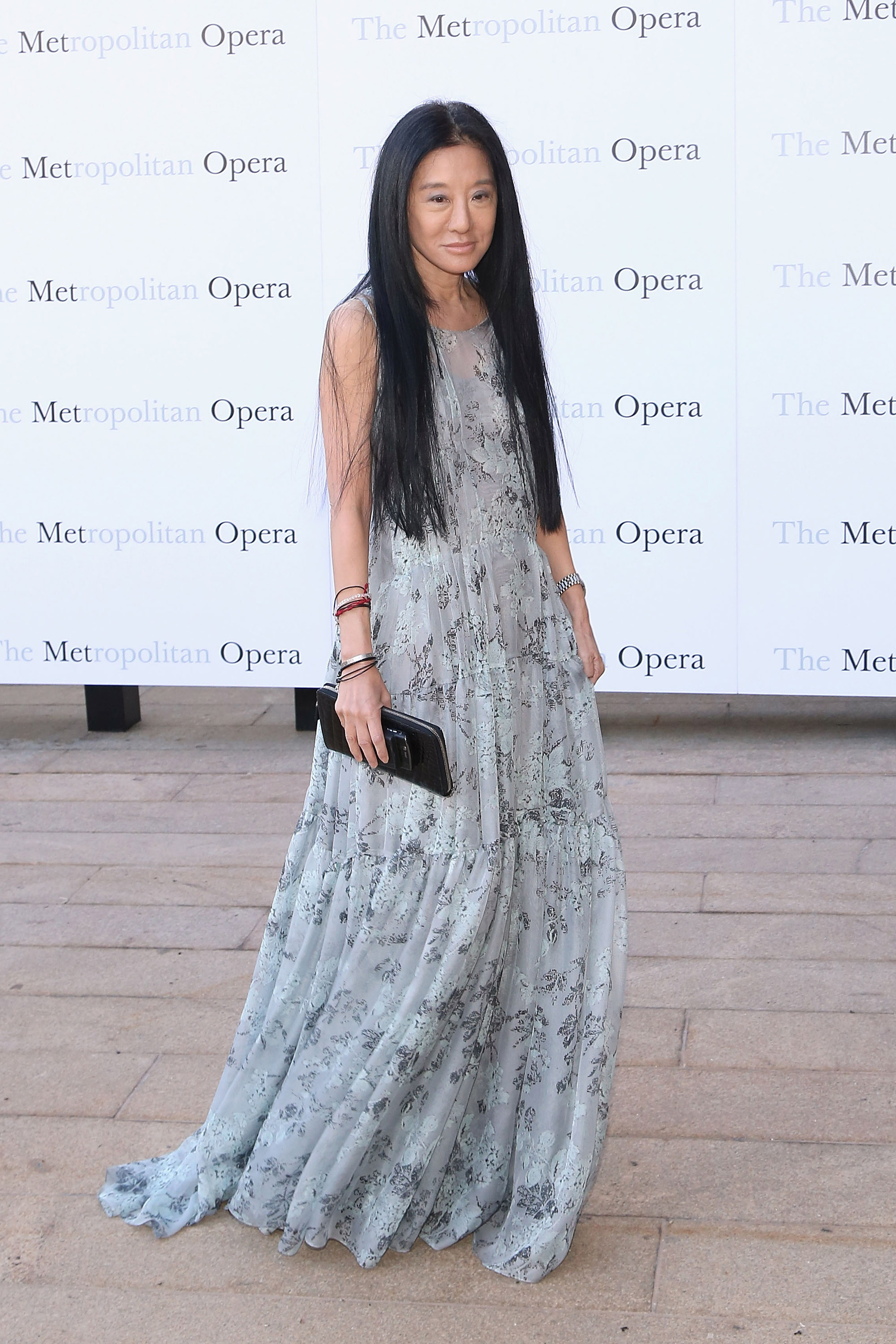 Attending the Metropolitan Opera's season opening, Vera Wang wears a soft blue-gray floral gown with a flowing silhouette. She pairs her look with layered bangles and a black clutch, creating an ethereal presence on the outdoor arrival path.
