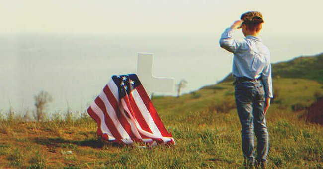 A kid saluting an american flag covering a grave | Source: Shutterstock