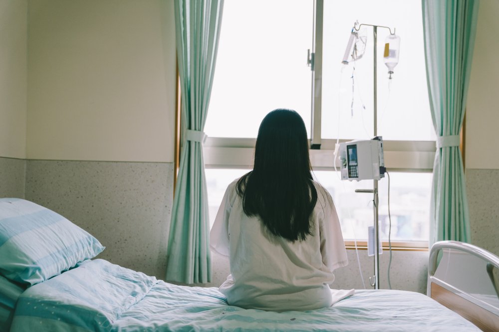 Frau sitzt auf dem Bett in einer Klinik. | Quelle: Shutterstock