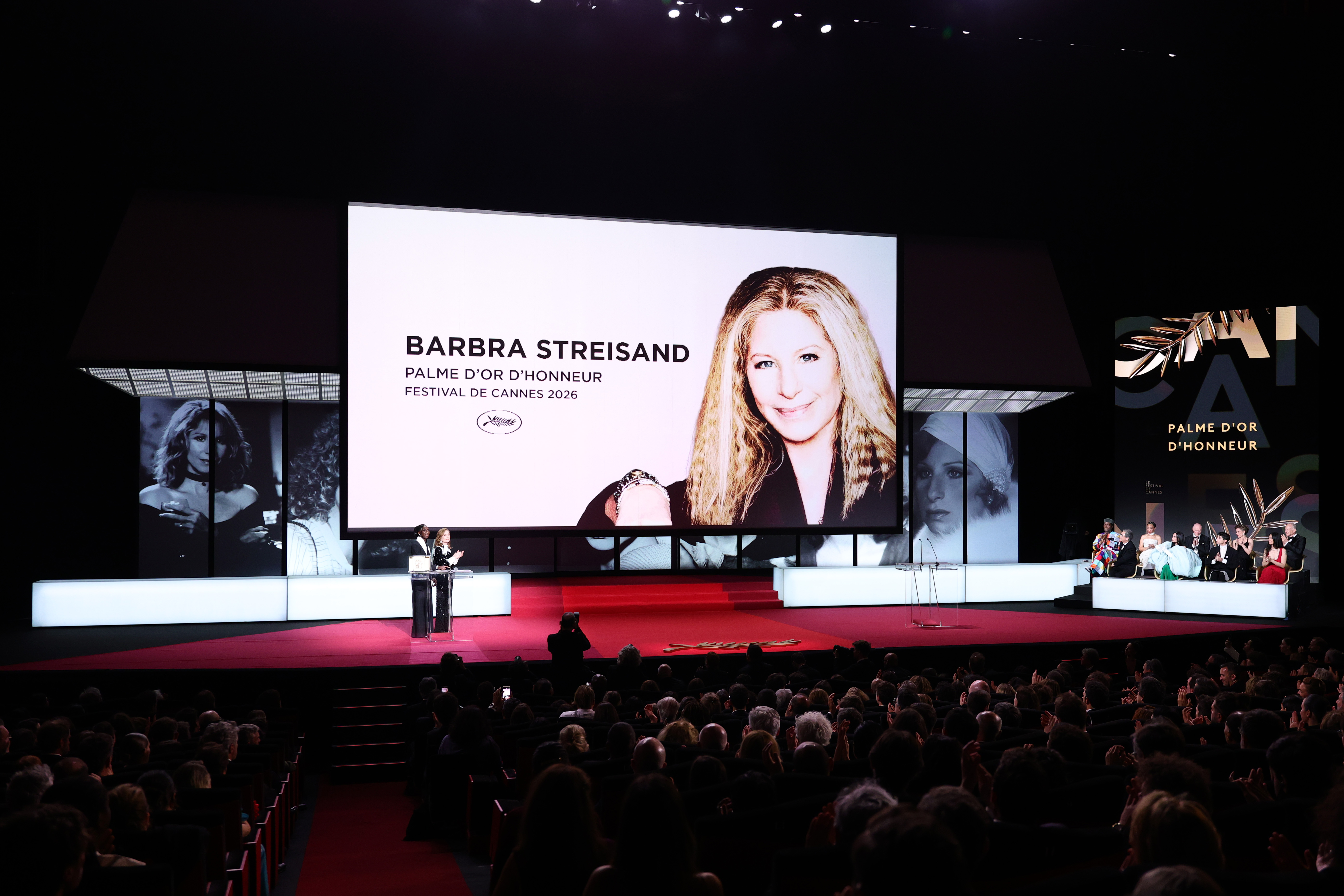 Isabelle Huppert accepts the Honorary Palme d'Or on behalf of Barbra Streisand from host Eye Haïdara on stage during the closing ceremony of the 79th annual Cannes Film Festival at Palais des Festivals on May 23, 2026 in France. | Source: Getty Images