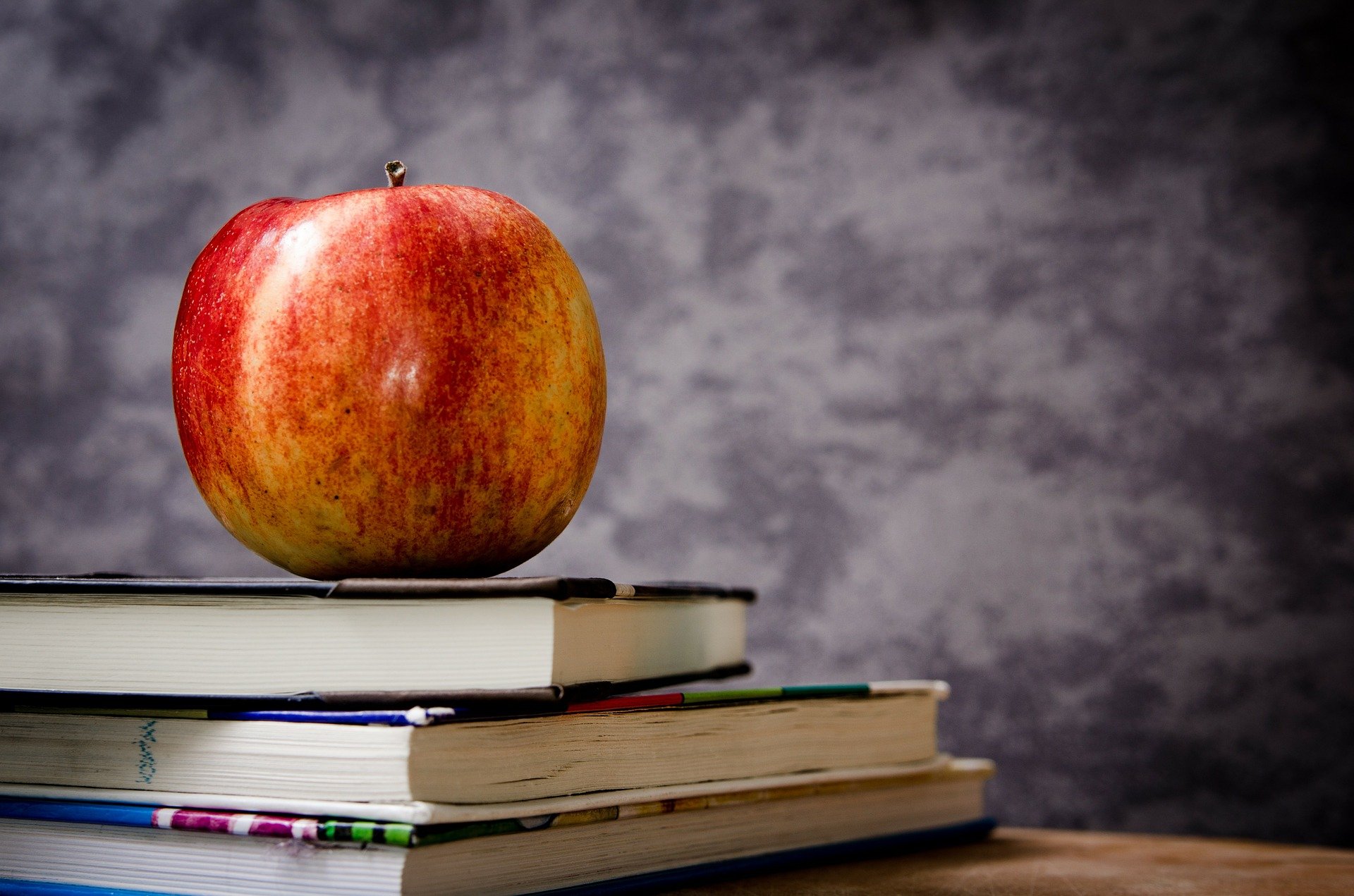 A red apple balanced on a pile of books. | Photo: Pixabay/Michal Jarmoluk
