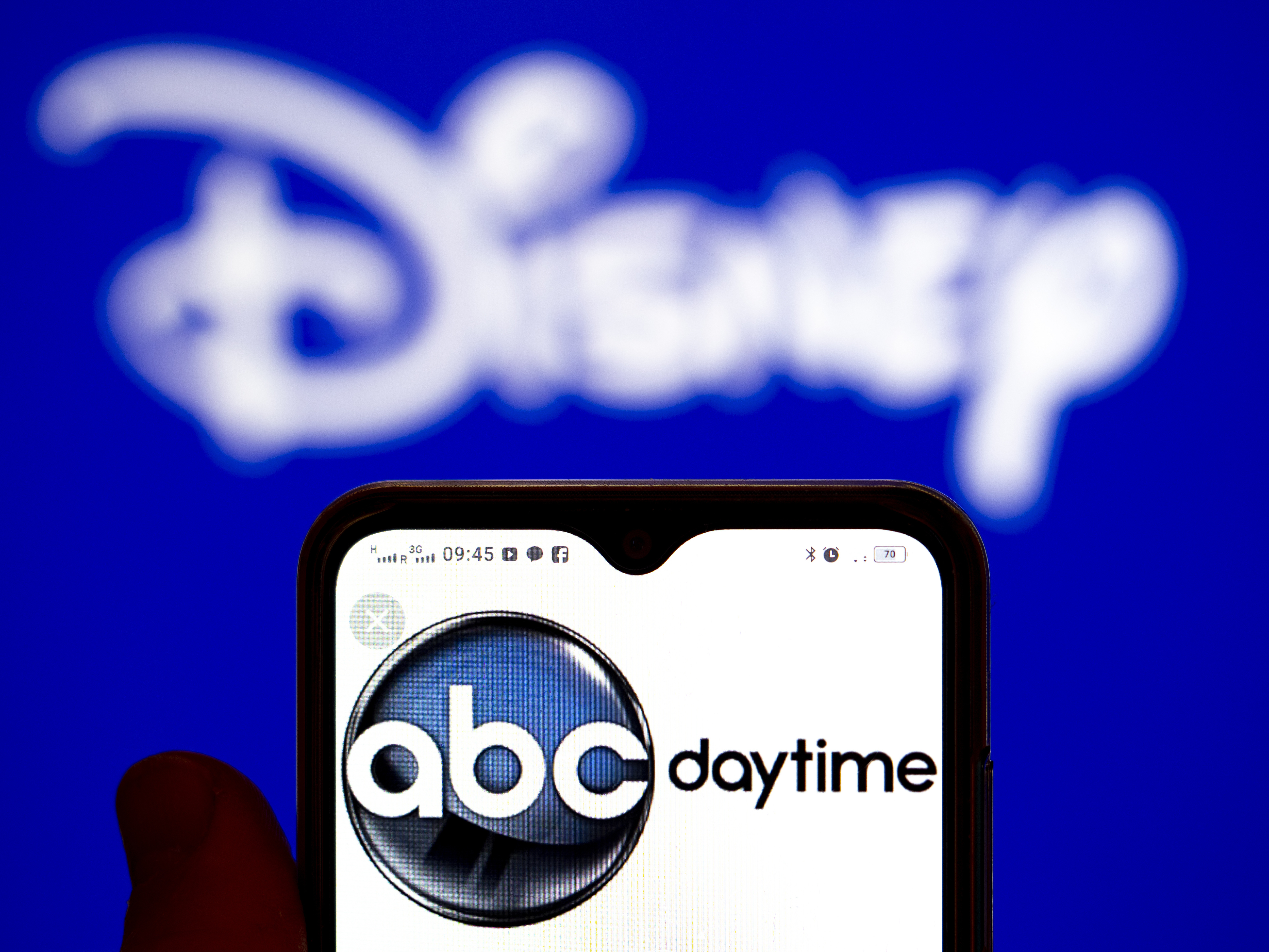 A photo of a person holding a phone with the ABC Daytime logo on it in front of a Disney sign taken in Ukraine on February 1, 2022. | Source: Getty Images