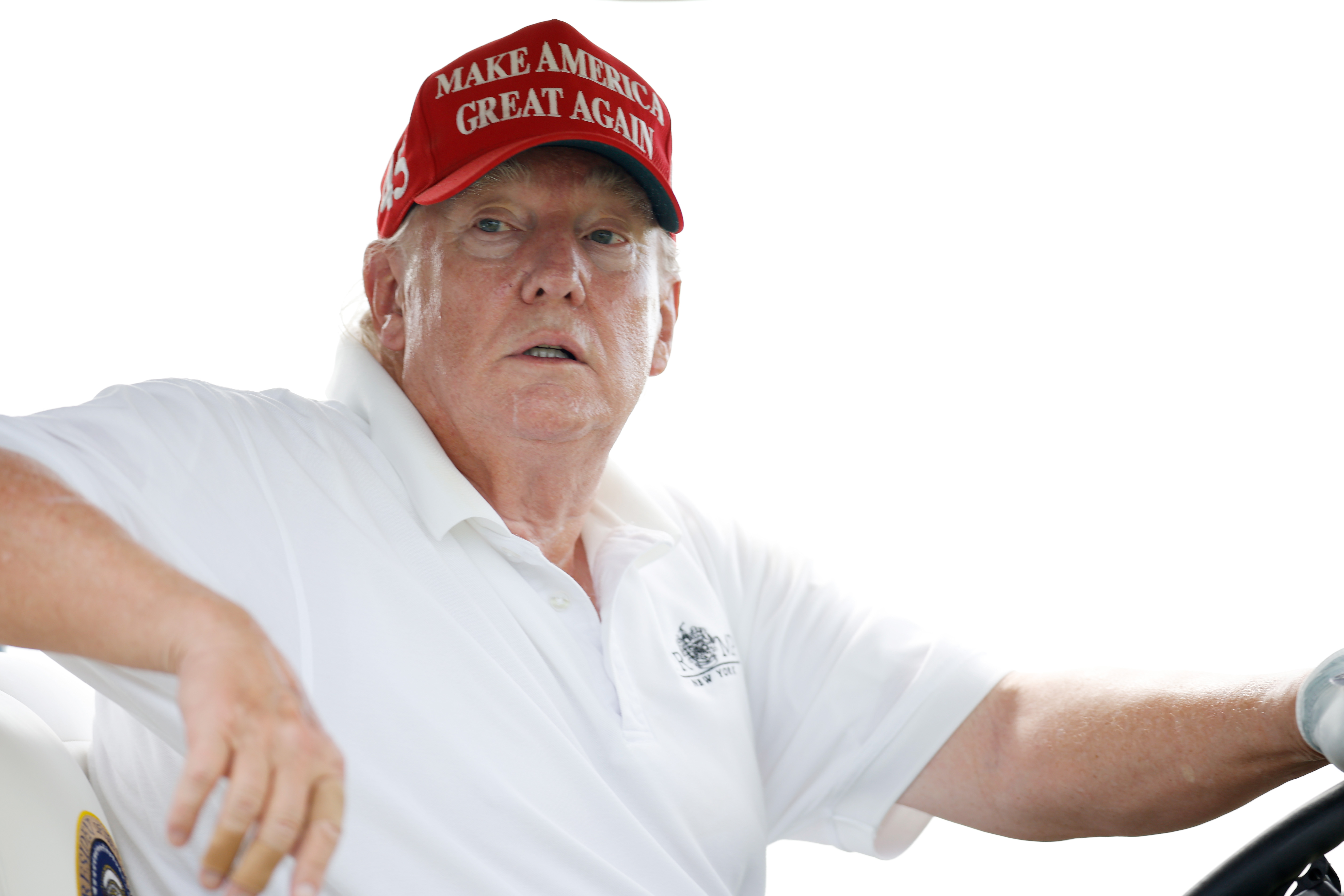 In a close-up as he drives the cart, Donald Trump's skin appears flushed around the cheeks and eyes, with paler areas near his ears and collar. His shirt remains open at the neck, revealing more contrast in tone.