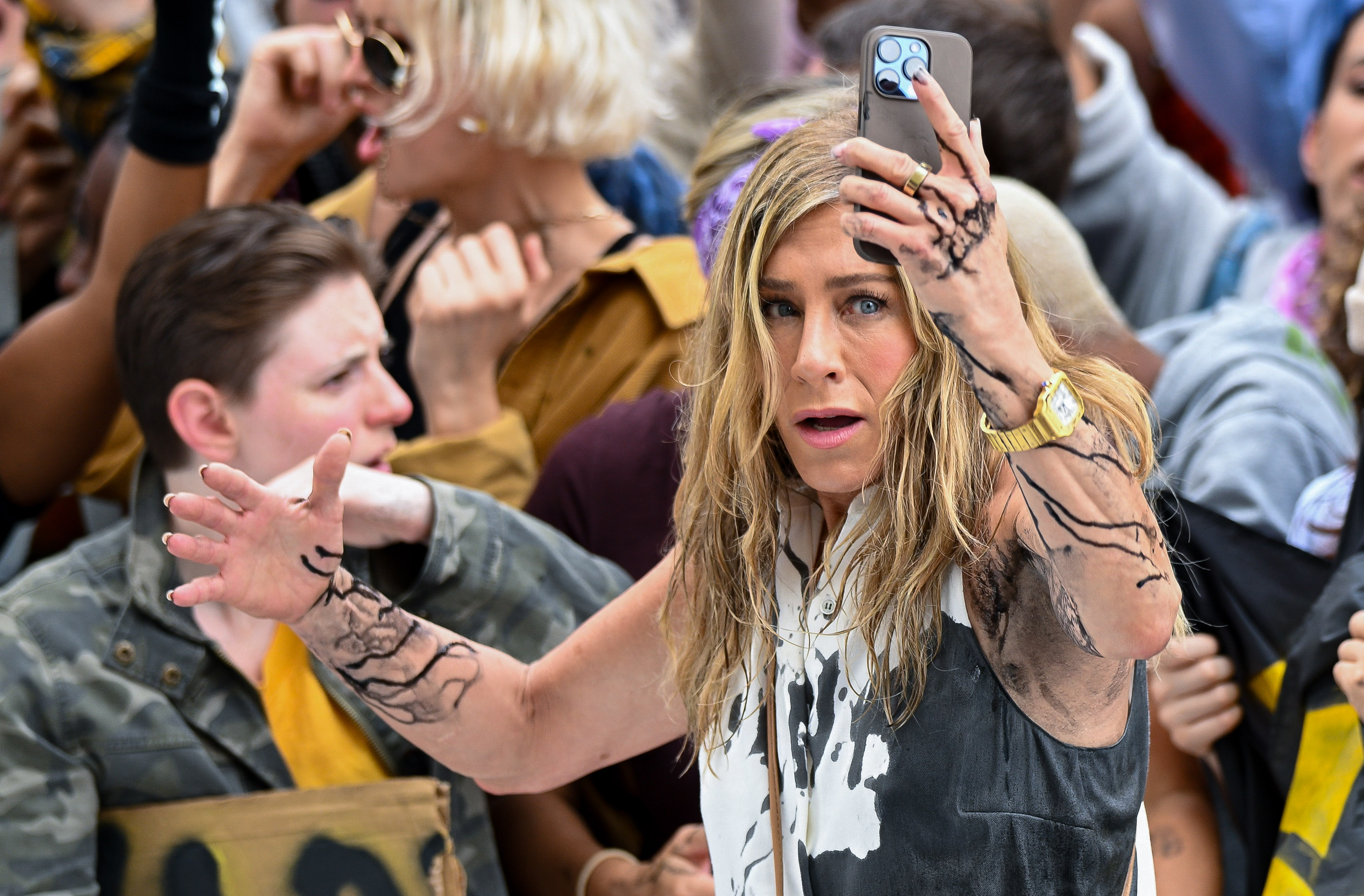 Jennifer Aniston holds her mobile phone while being covered with black oil in the Flatiron District of New York City on July 28, 2024 | Source: Getty Images