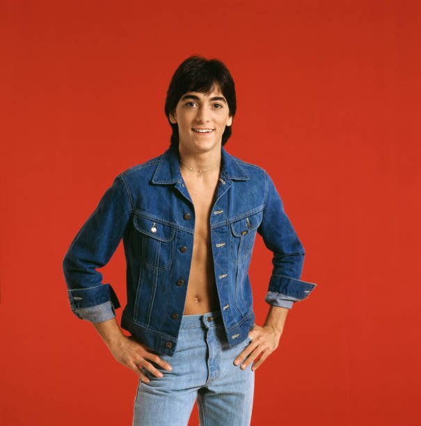 Scott Baio pictured with his hands on his hips, wearing a jean jacket with no shirt underneath, paired with jeans. / Source: Getty Images