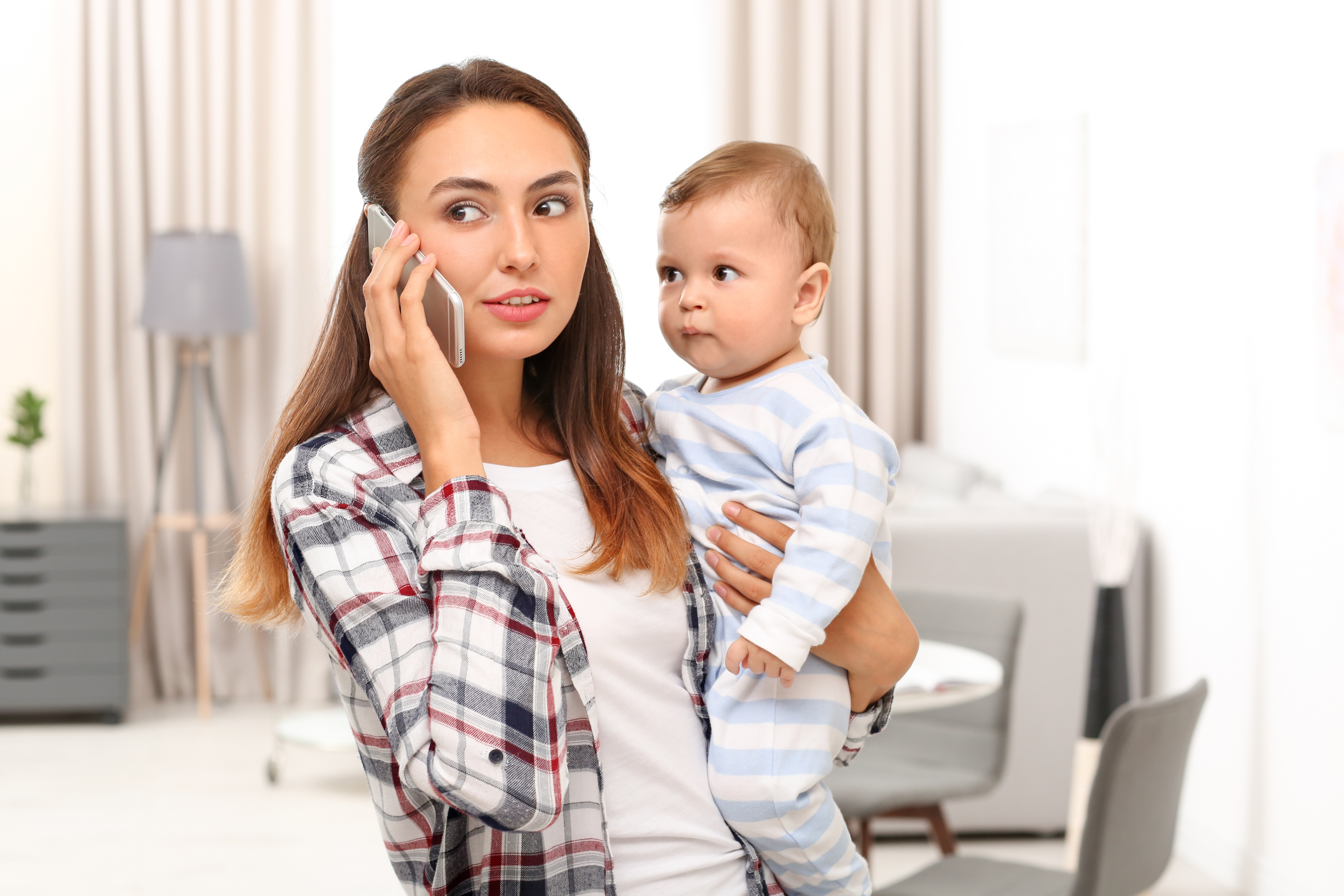 A young mother holding her baby while talking on the phone | Source: Shutterstock