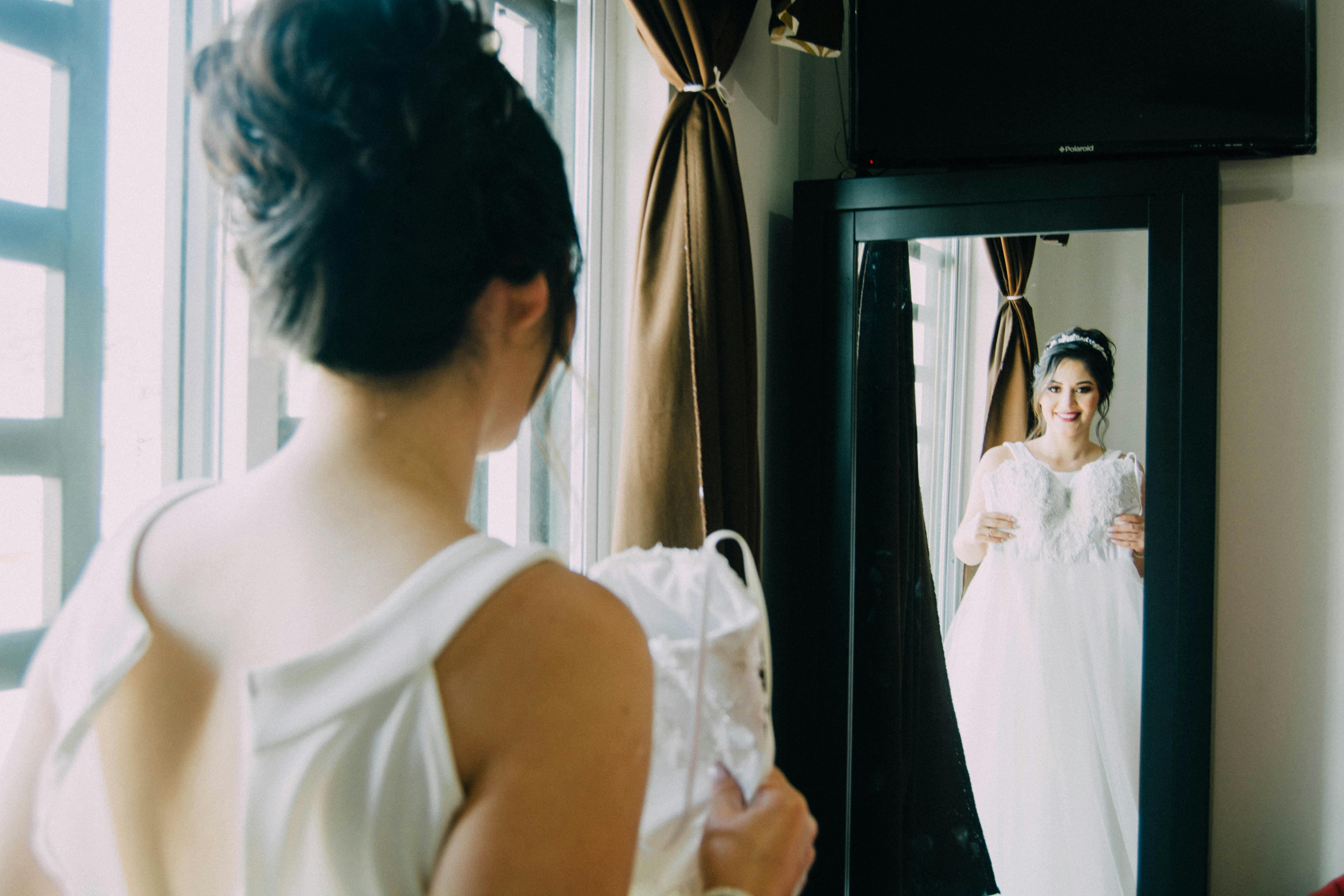 A happy bride holding her wedding dress while looking in a mirror | Source: Pexels