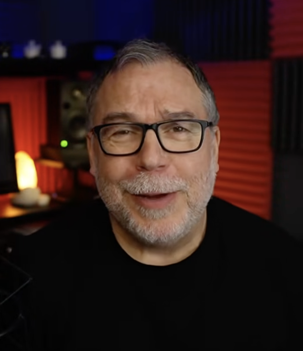 A greying but still-sharp Brookstein, now sporting black-framed glasses and a neat salt-and-pepper beard, addresses the camera directly from what appears to be a home recording studio, red acoustic panels visible behind him — a still from his first YouTube video in five years, posted in April 2022. | Source: YouTube/stevebrookstein