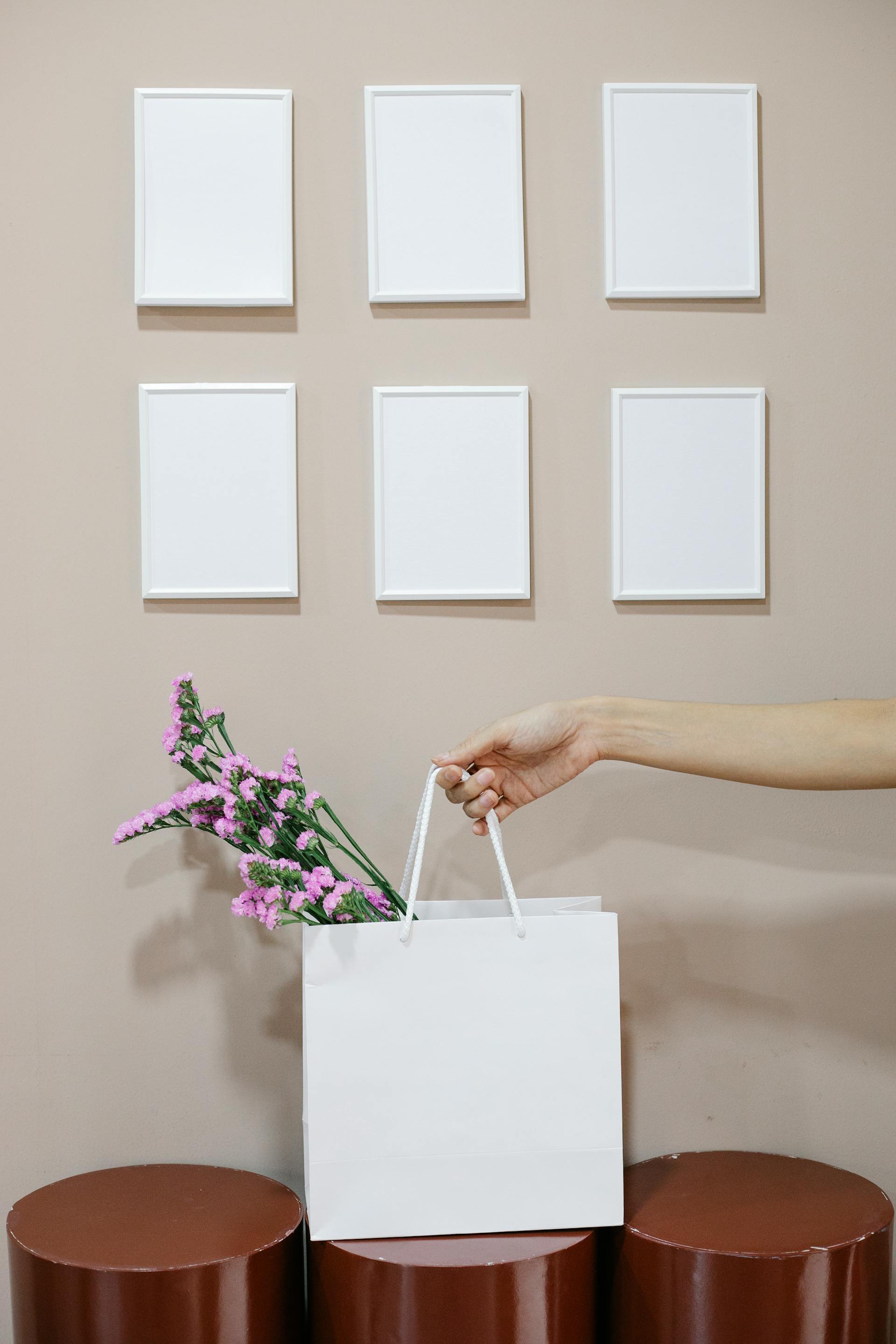 A close-up photo of a woman holding a paper bag with flowers near a wall with blank frames | Source: Pexels