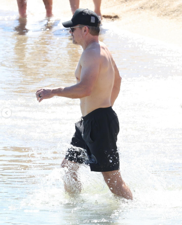 Matt Damon walks at the beach in black shorts, cap, and sunglasses, posted in July 2024. | Source: Instagram/justjared