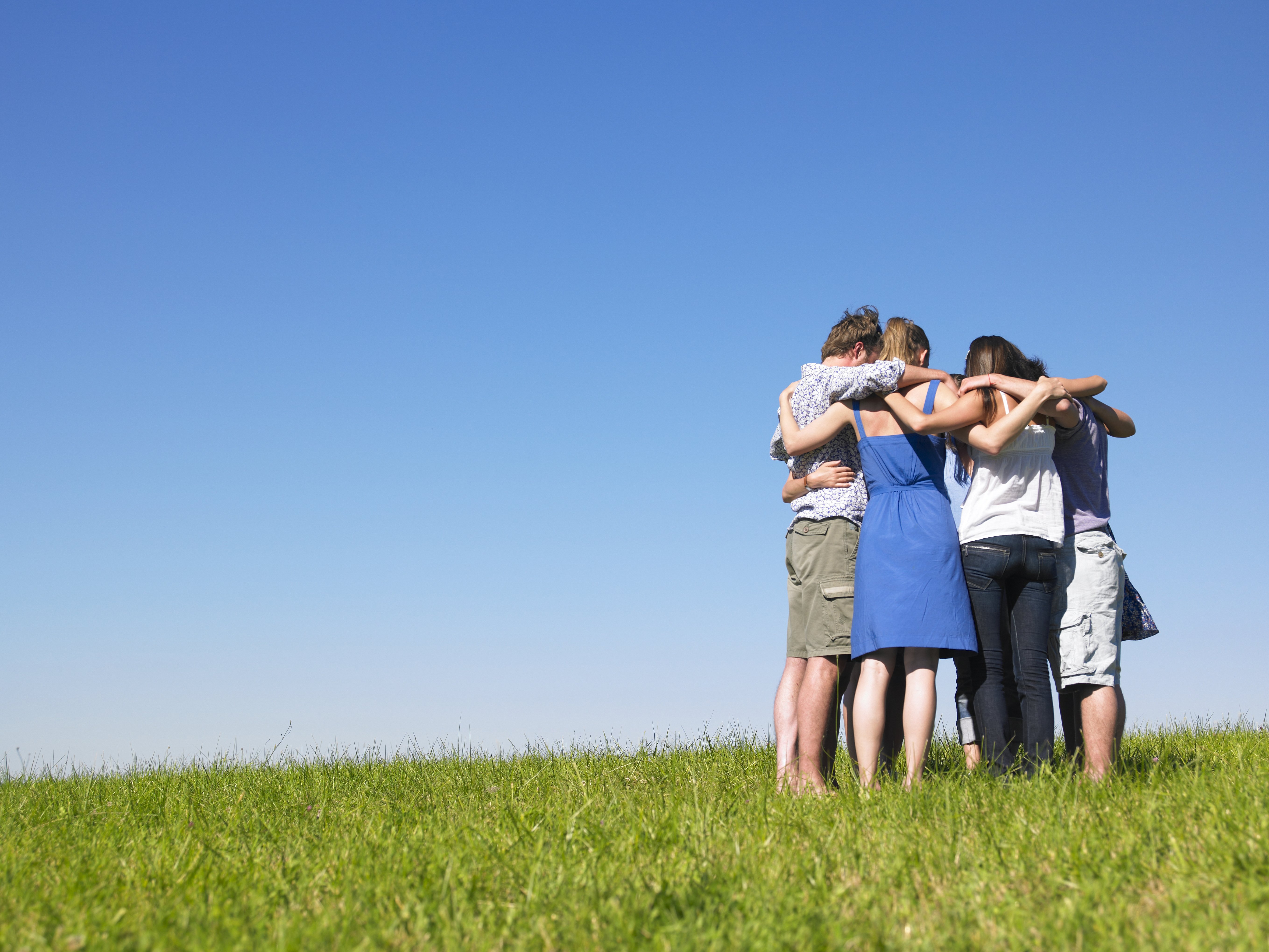 A group of people hugging in a field. │Source: Shutterstock