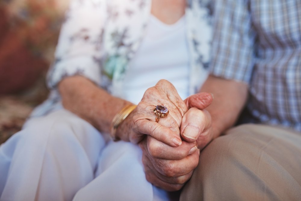 Cropped shot of elderly couple holding hands while sitting together at home. | Photo: Shutterstock